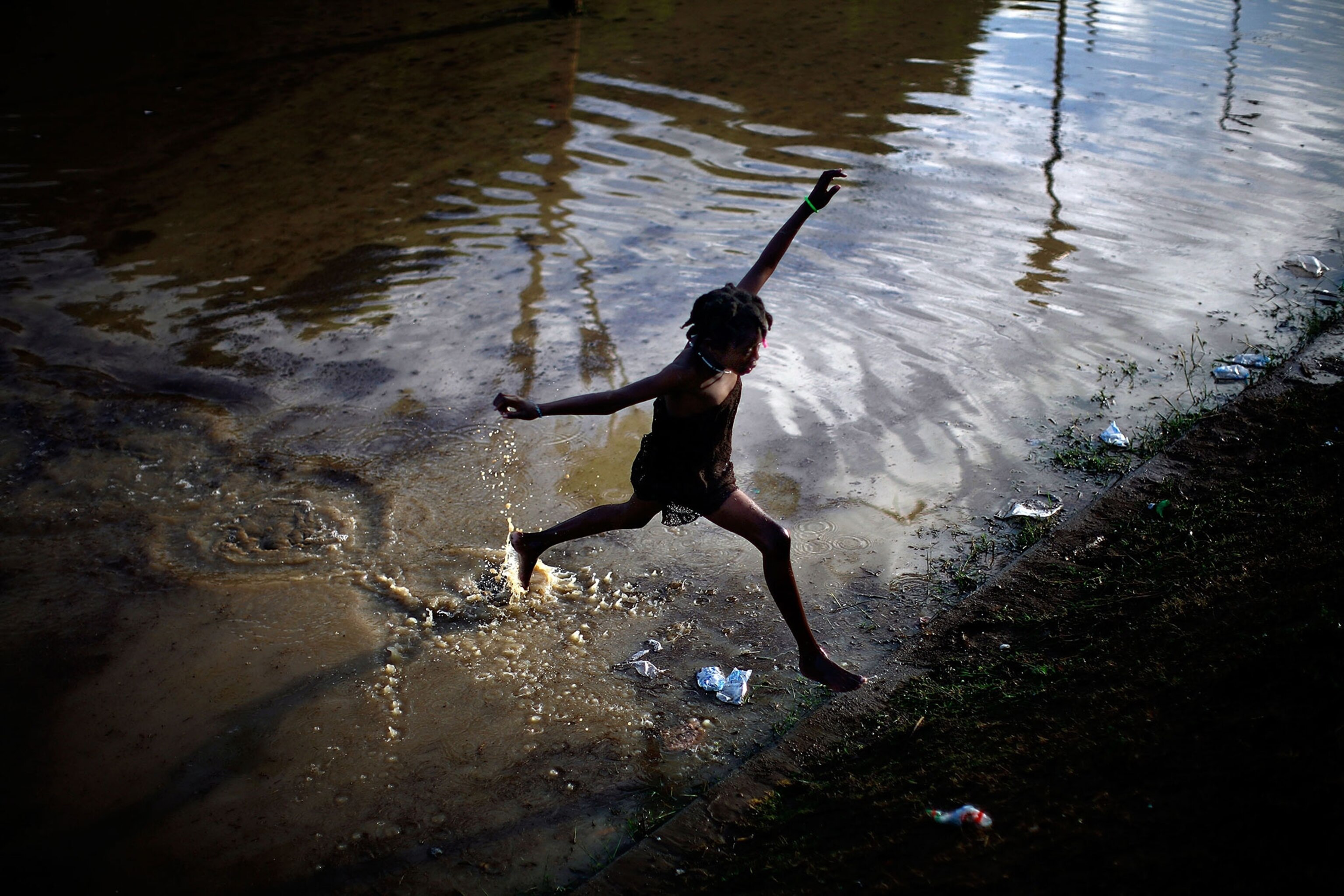 a little girl jumps across a flooded field containing the sewage runoff