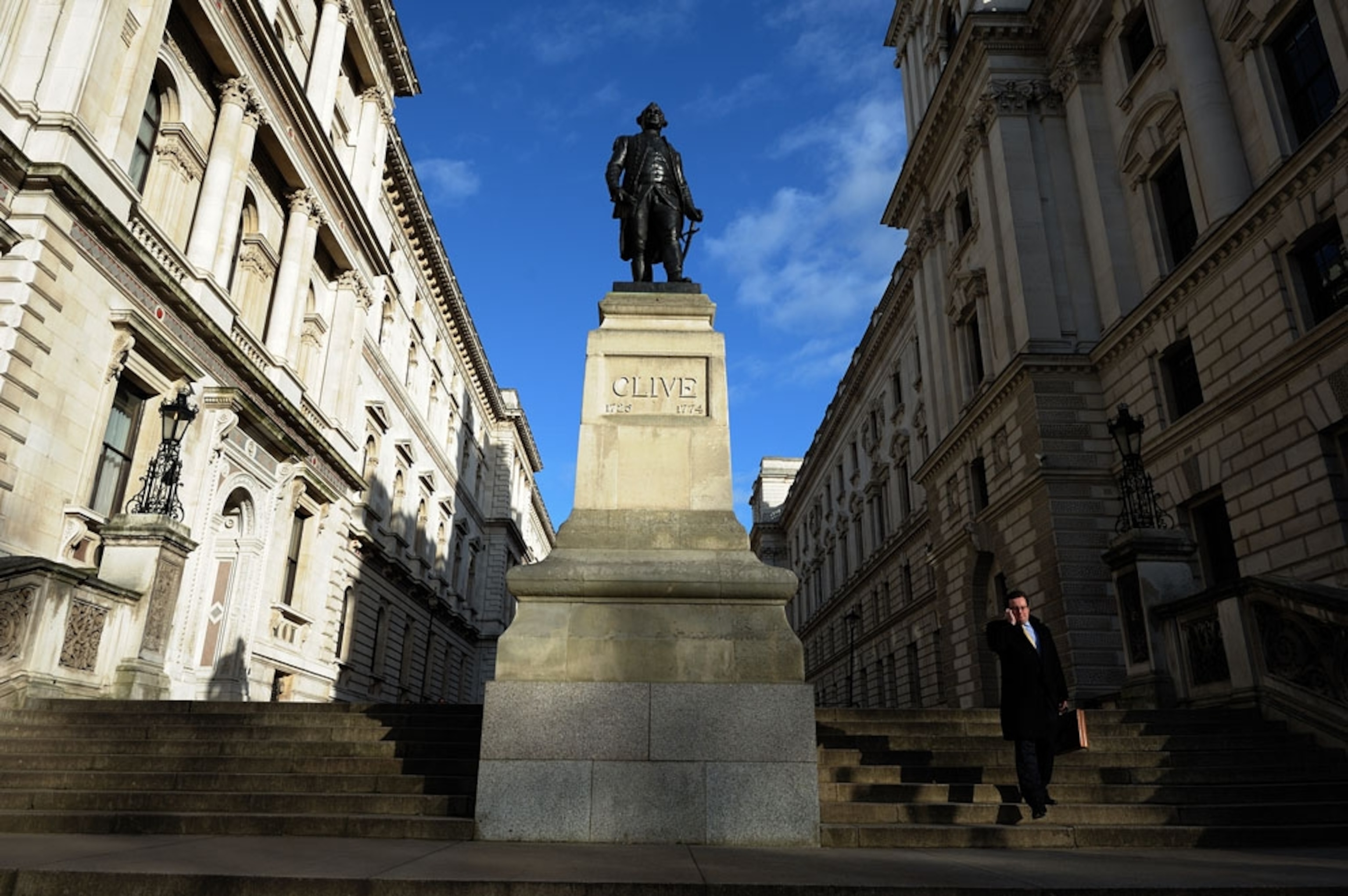 A man walking past a statue of Robert Clive in London