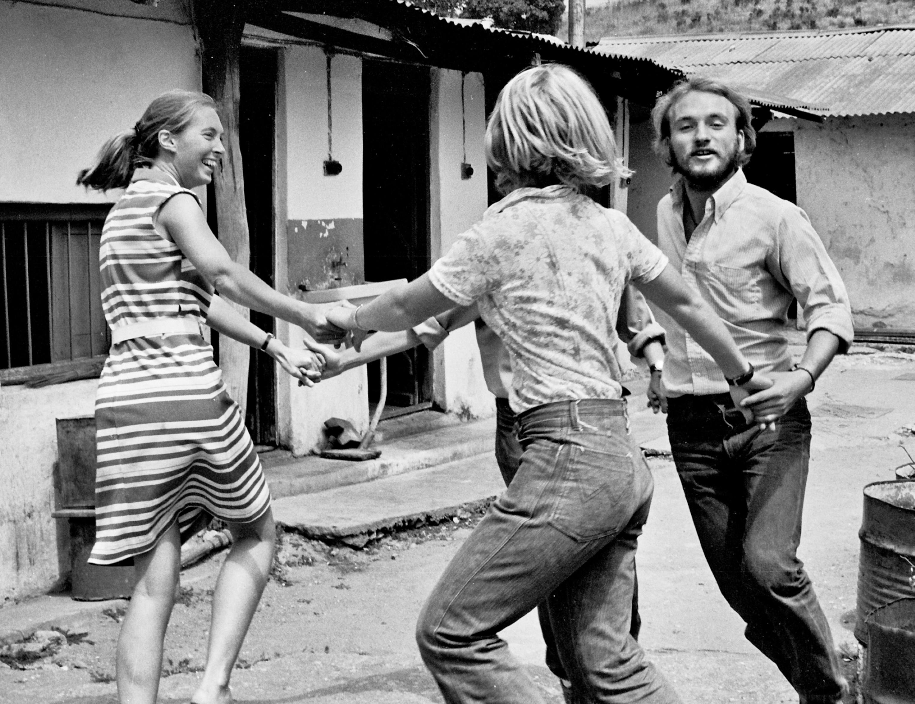 B&W photo of two young men and one woman dancing in circle.
