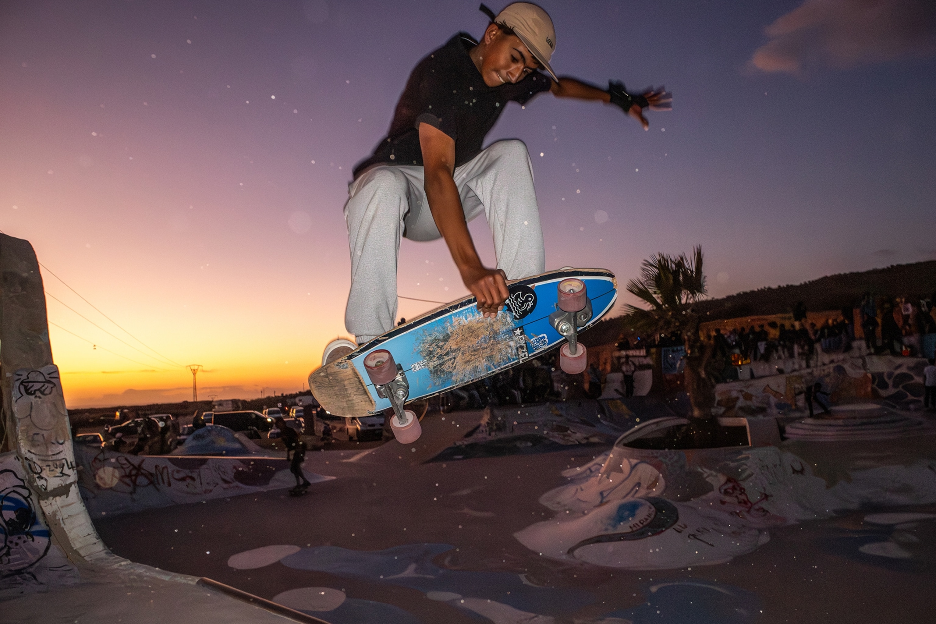 A teenager boy performing a skateboard stunt in a skate park at sunset.