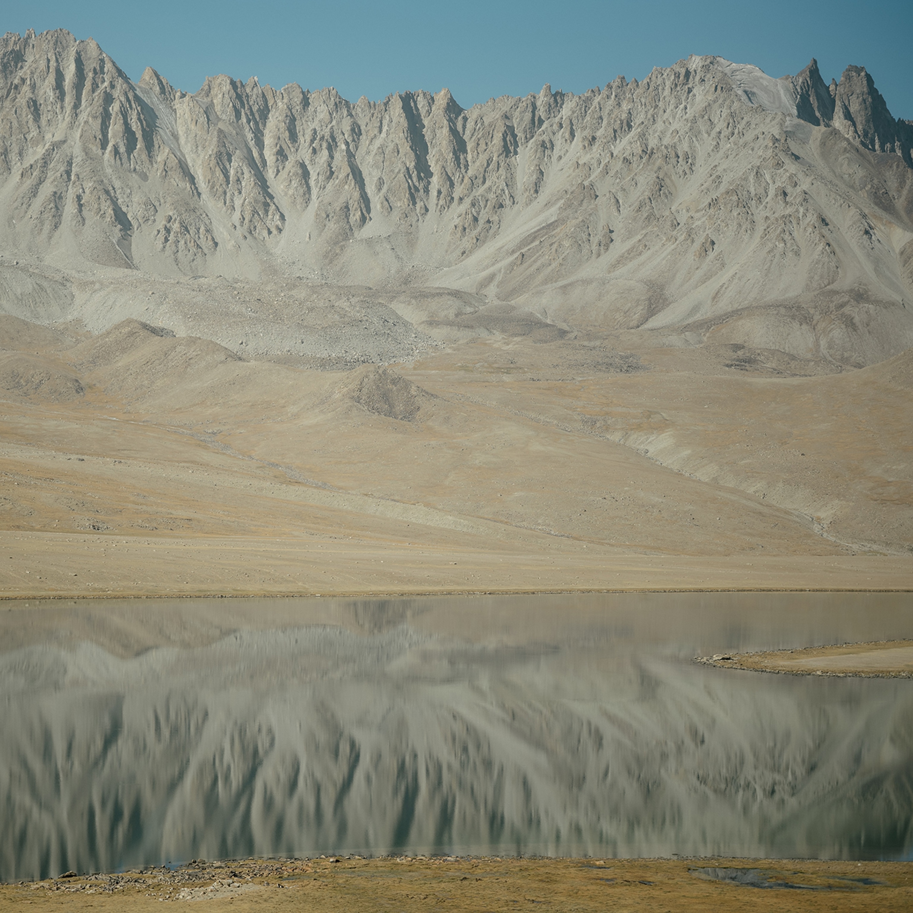 Tall grey and brown mountains reflect onto a lake in the foreground.