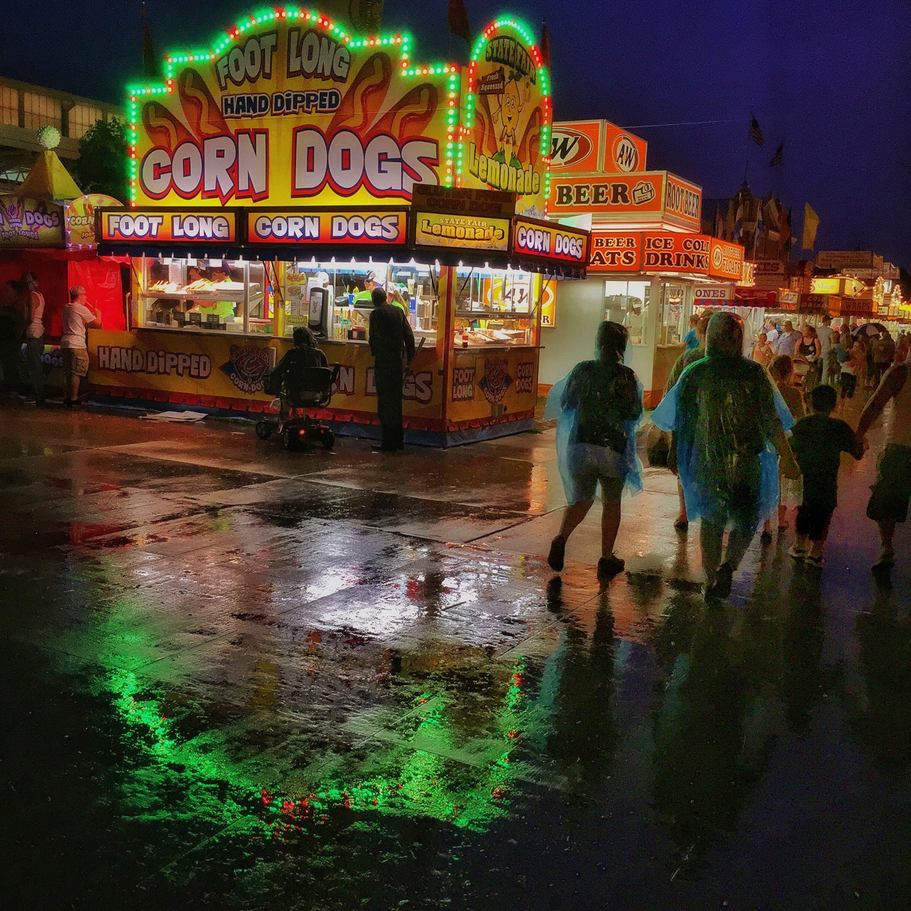 a rainy night in Des Moines, state fairgoers stroll past refreshment stands