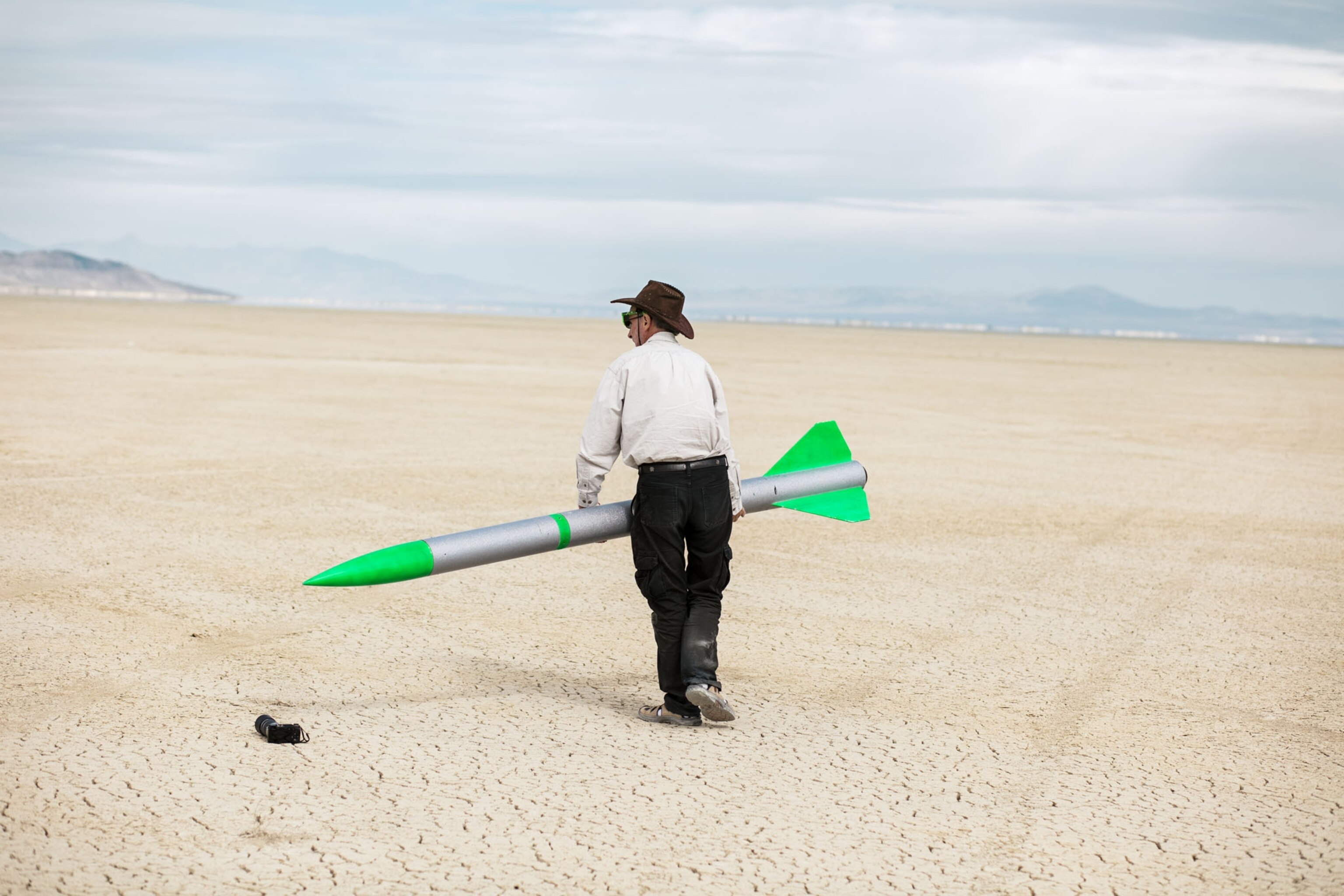a man walking in the desert carrying a gray and green rocket