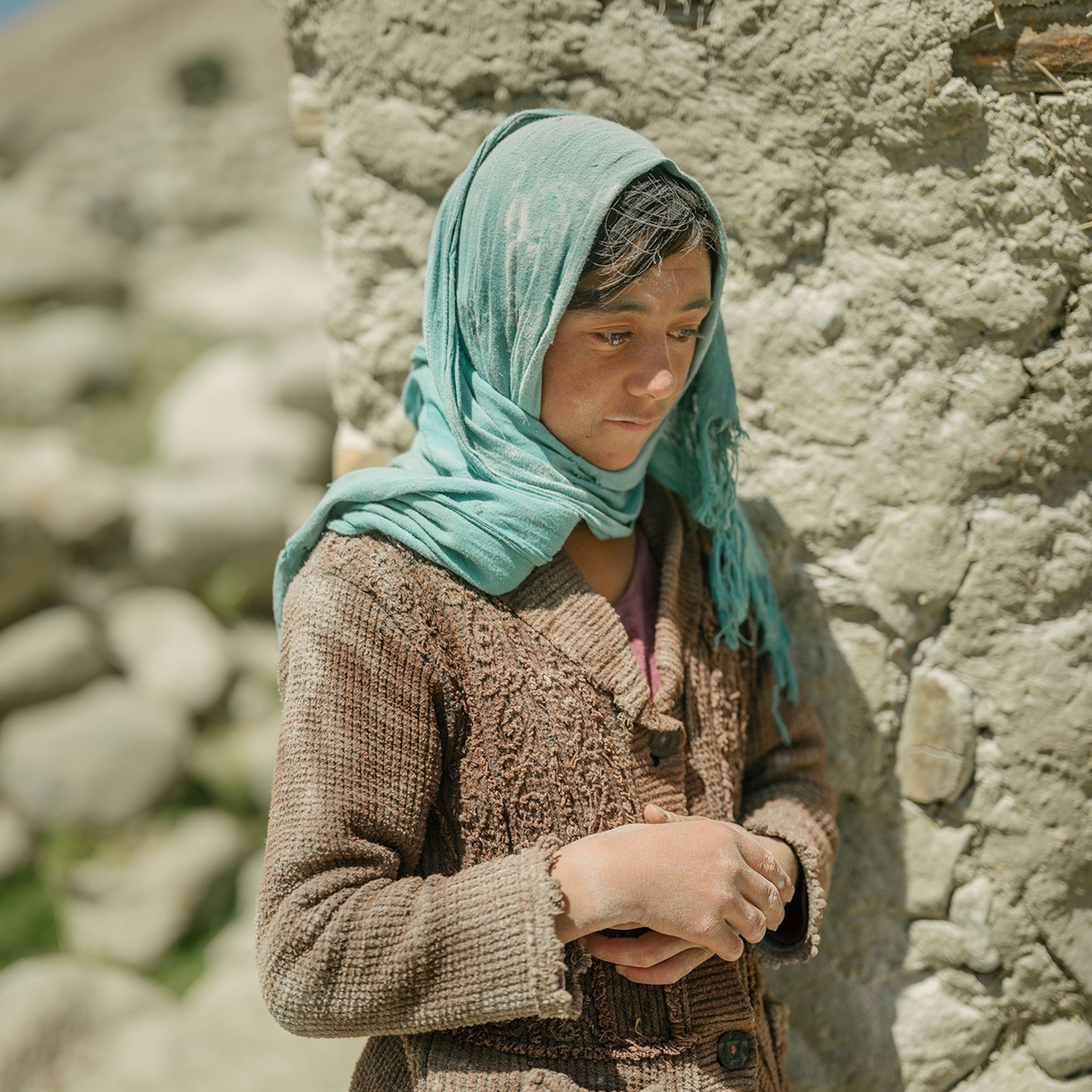 Portrait of a child standing near a wall looking down with there hands resting at their stomach.