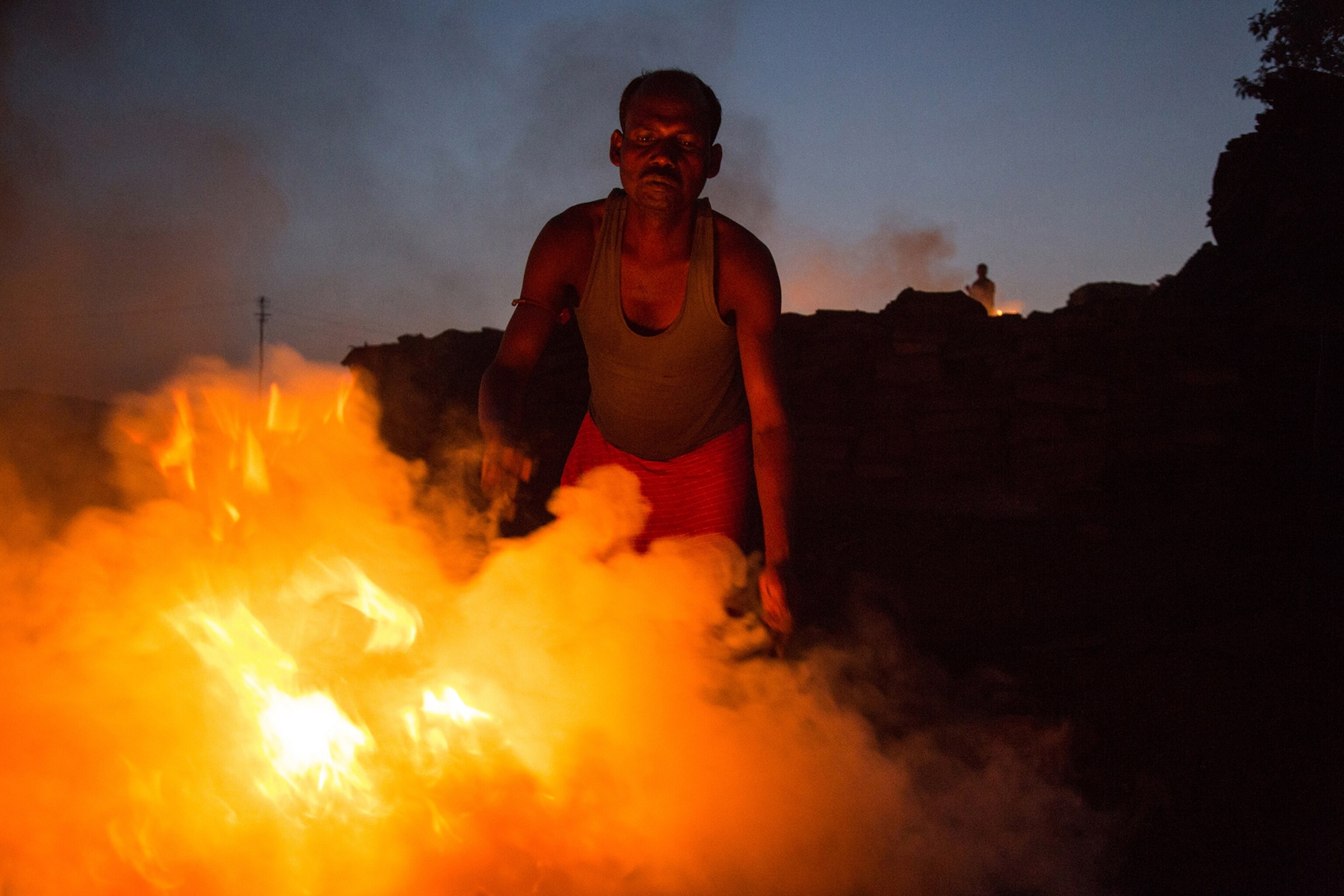 Jharkhand. India. A coal miner tends a fire in the mining camp where he lives with his family.