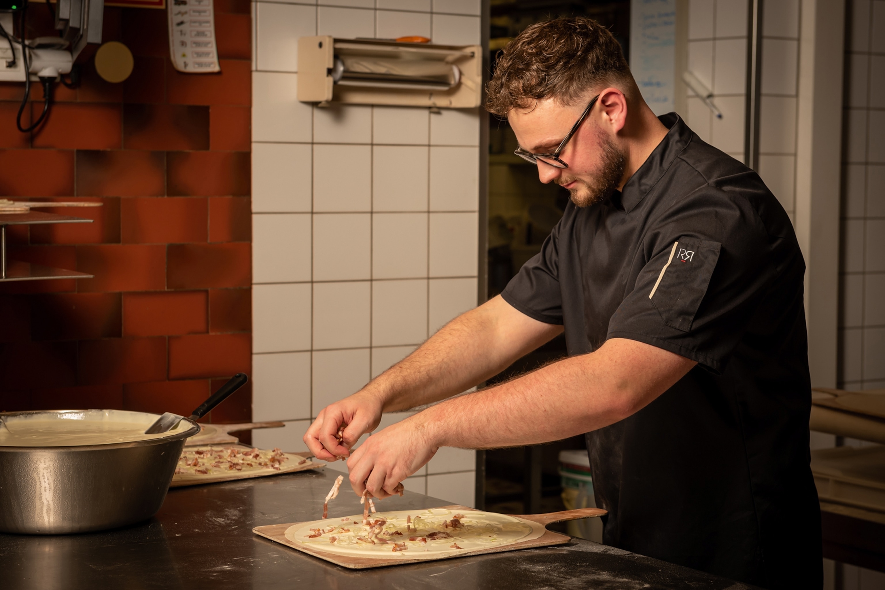 A young chef adding ham bits on top a thin dough with cream cheese.
