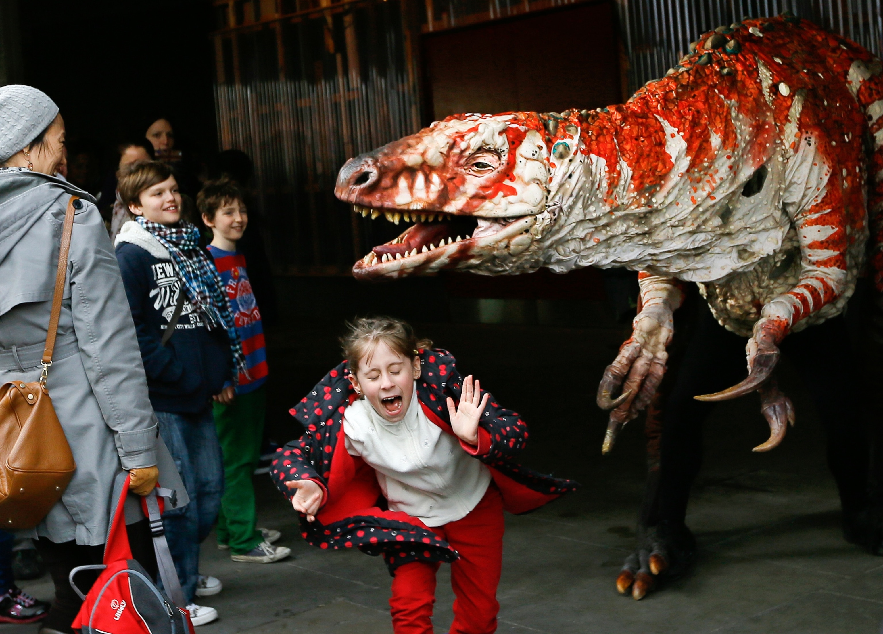children reacting to a performer playing a dinosaur, London