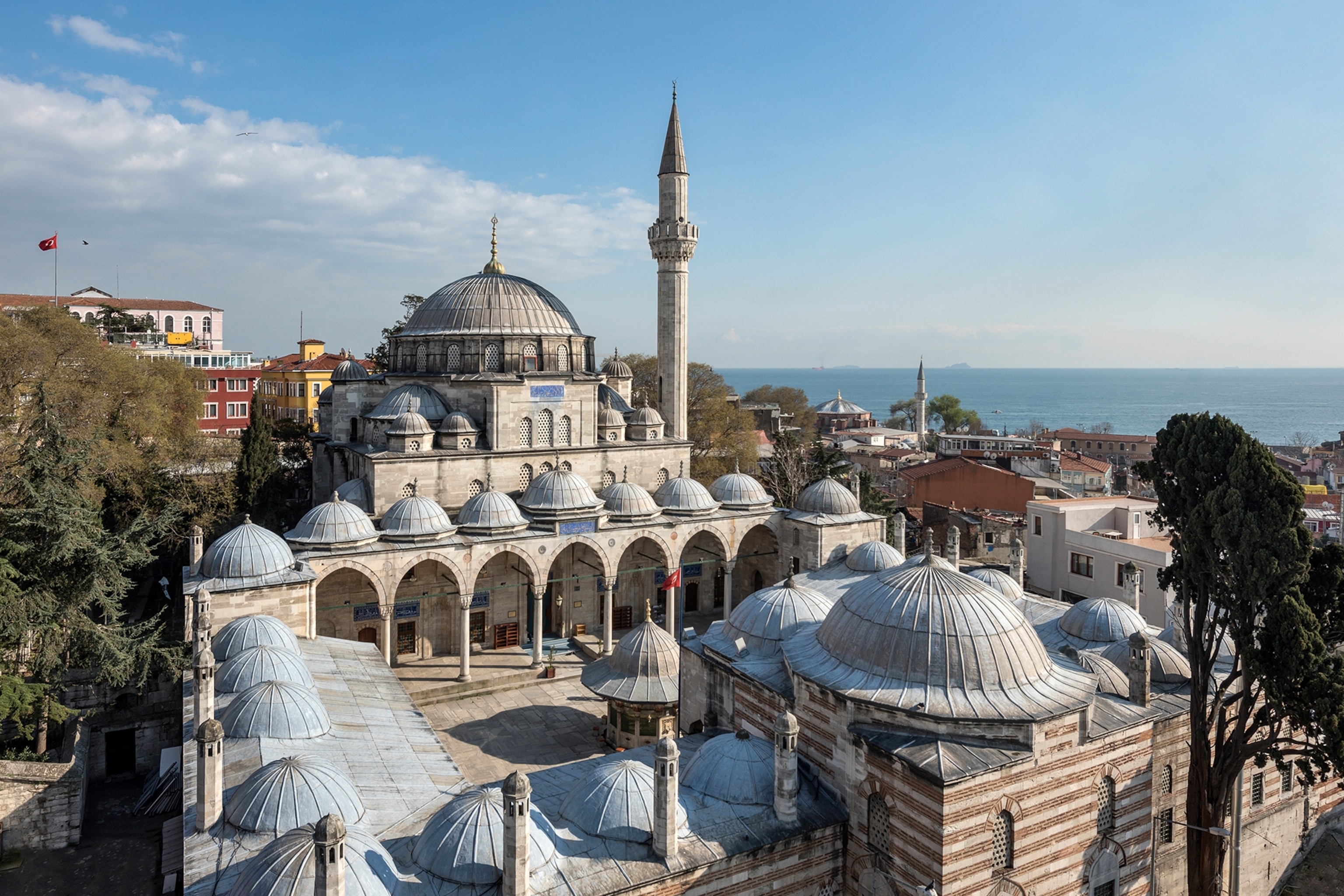 A birds-eye view onto the urban grounds of a palace with domed features and surrounded by a city mouthing into the ocean.