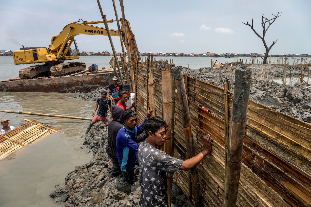 Men hold bamboo fencing to hold mud on a flooded cemetery.