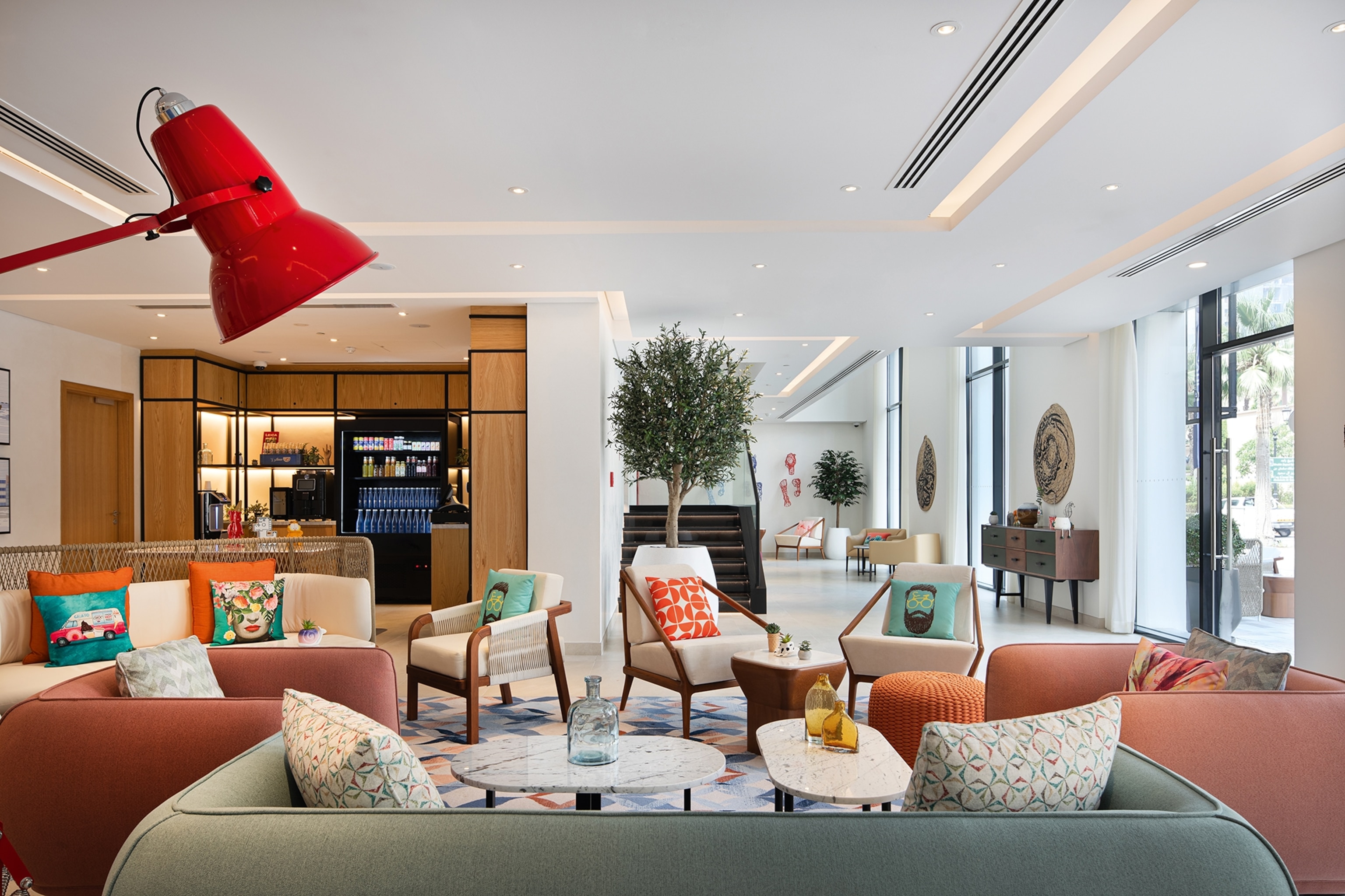 An eclectically designed hotel foyer with a seating lounge of multiple chairs and sofas, pattered cushions and small trees in corners.