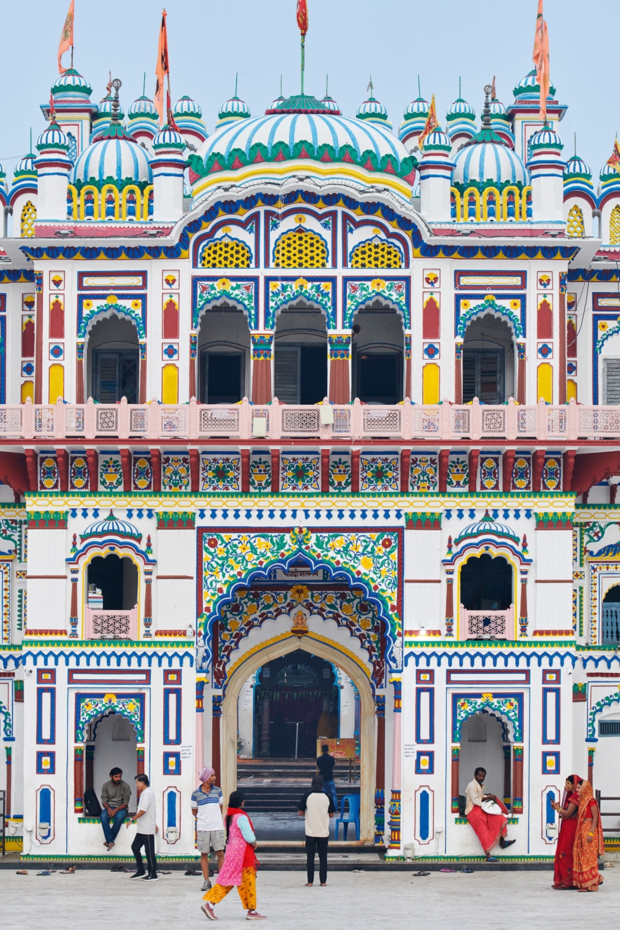 The entrance of a colourful and highly decorated temple with scalloped gateways and ornate paintings on the facade.