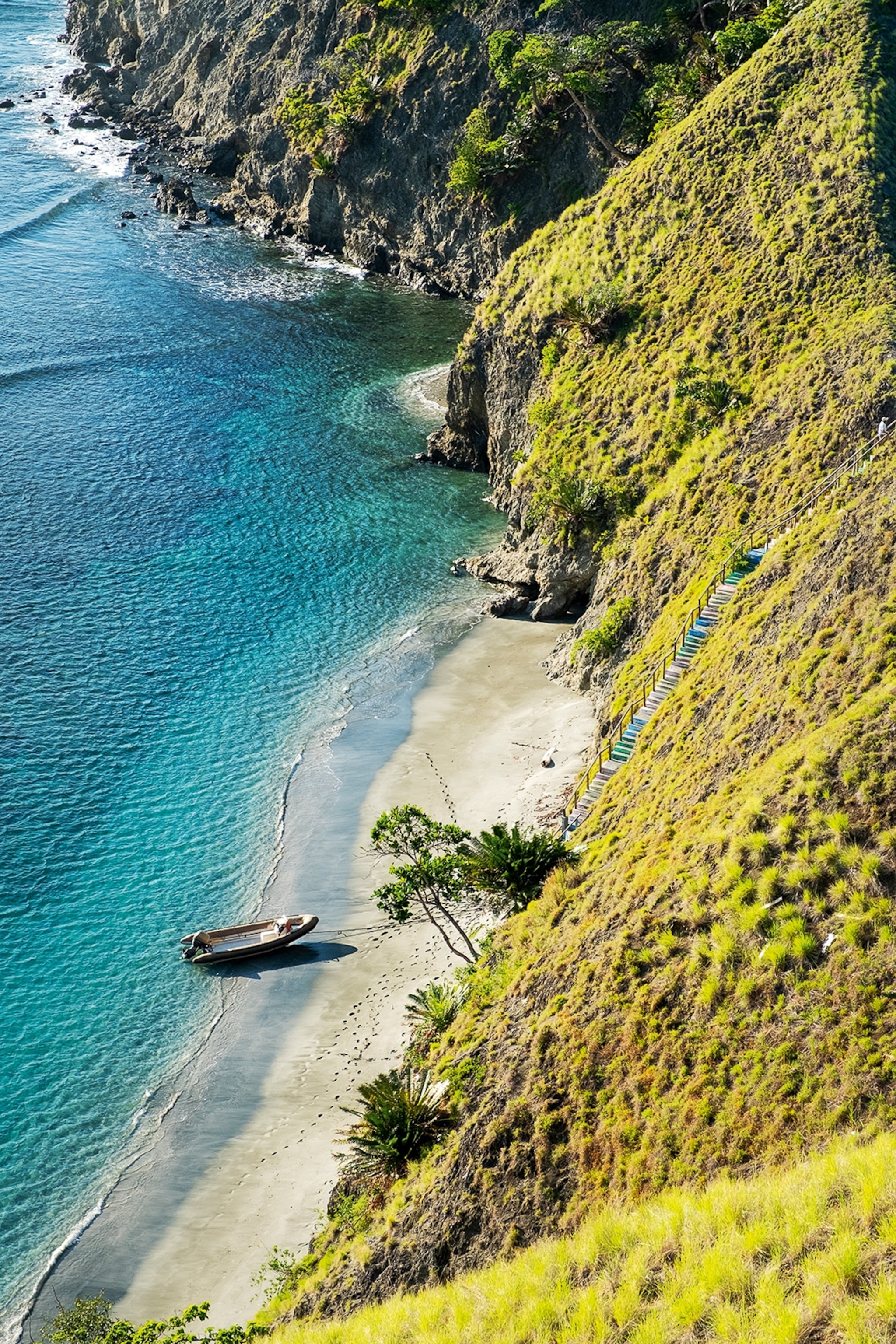 A small sand beach with a wooden fishing boat and footsteps leading to stairs leading up the steep hill enclosing the beach.