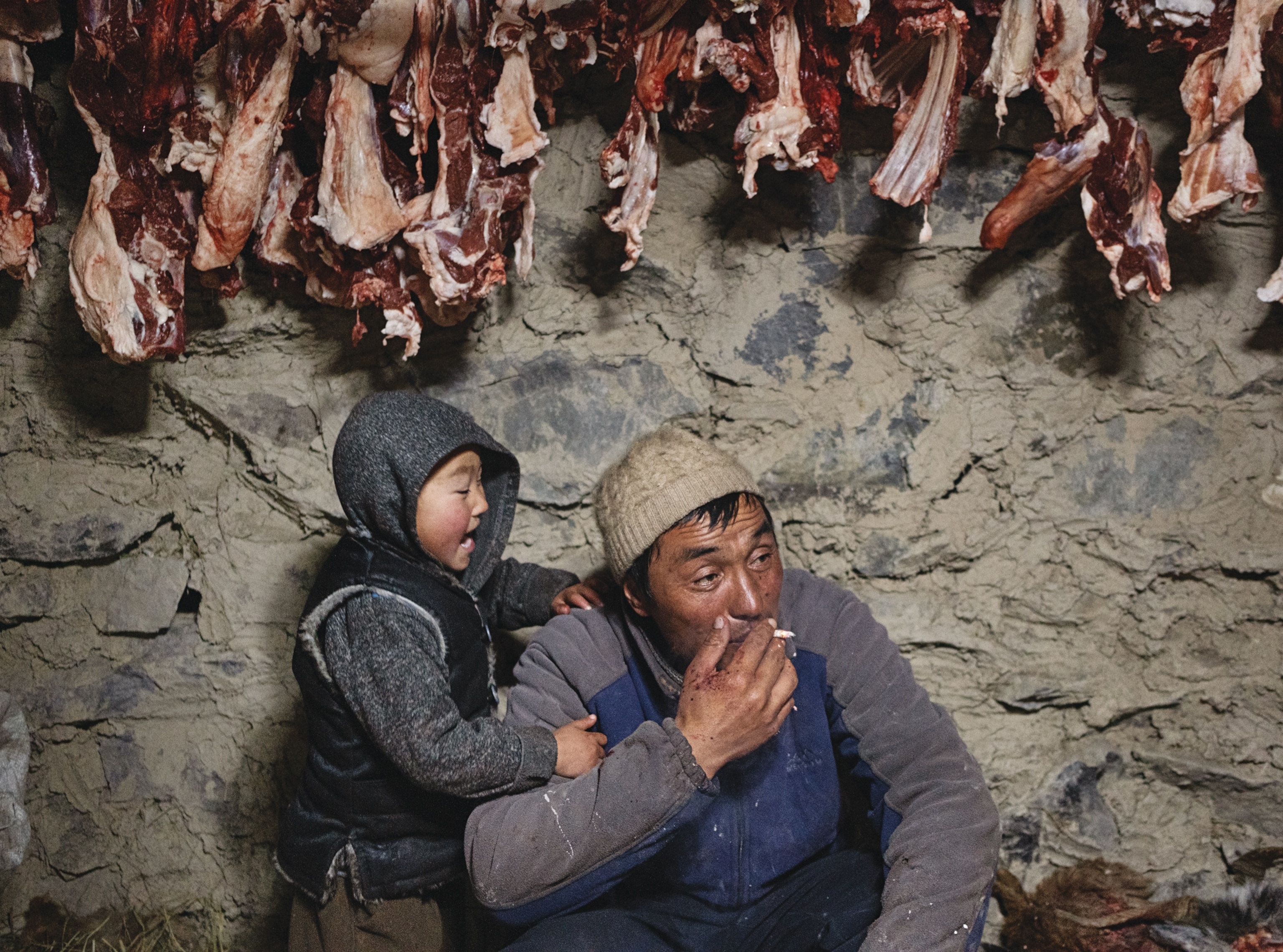 Man and child under handing to dry pieces of butchered meat.