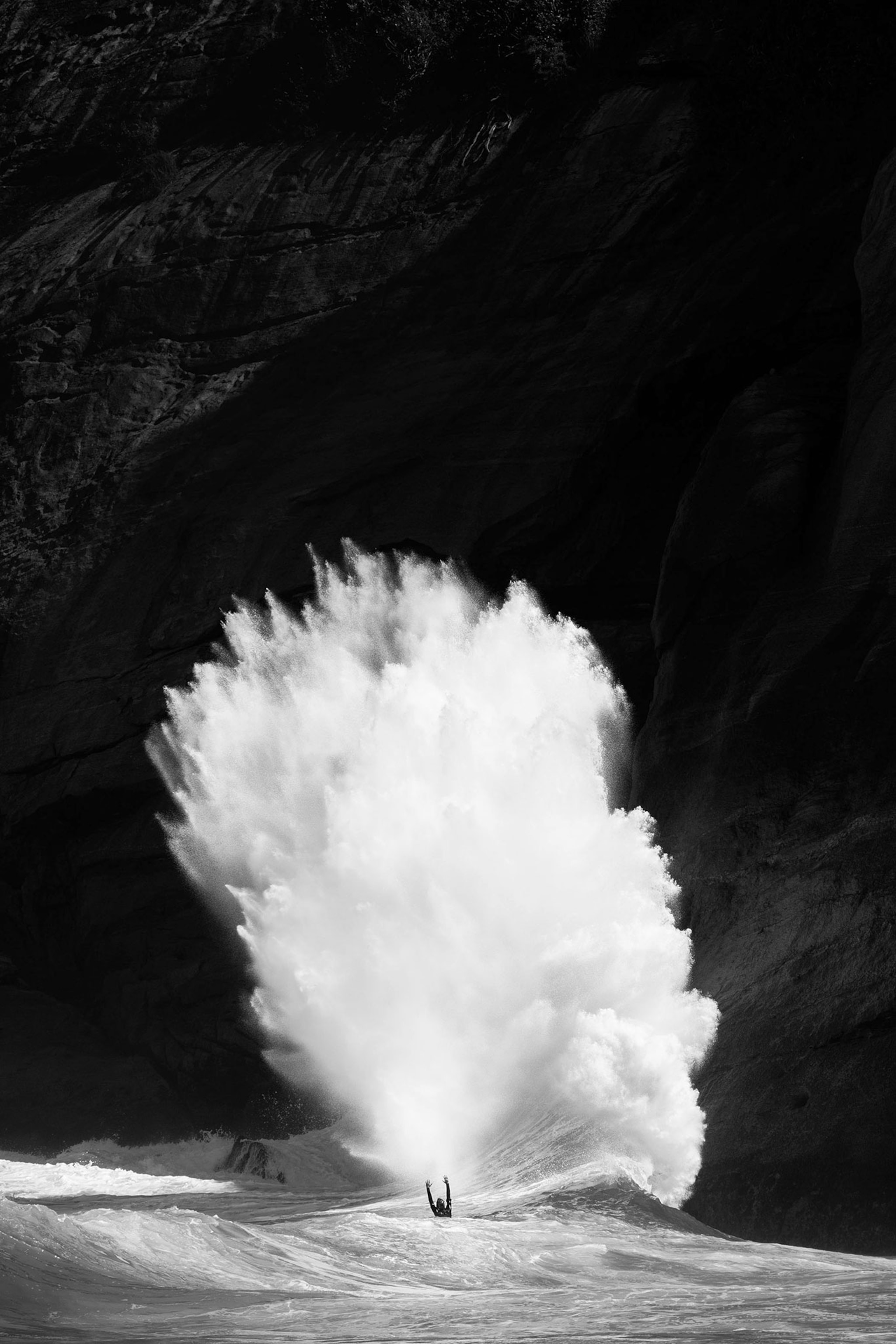 a surfer next to a giant wave crashing up against rocks