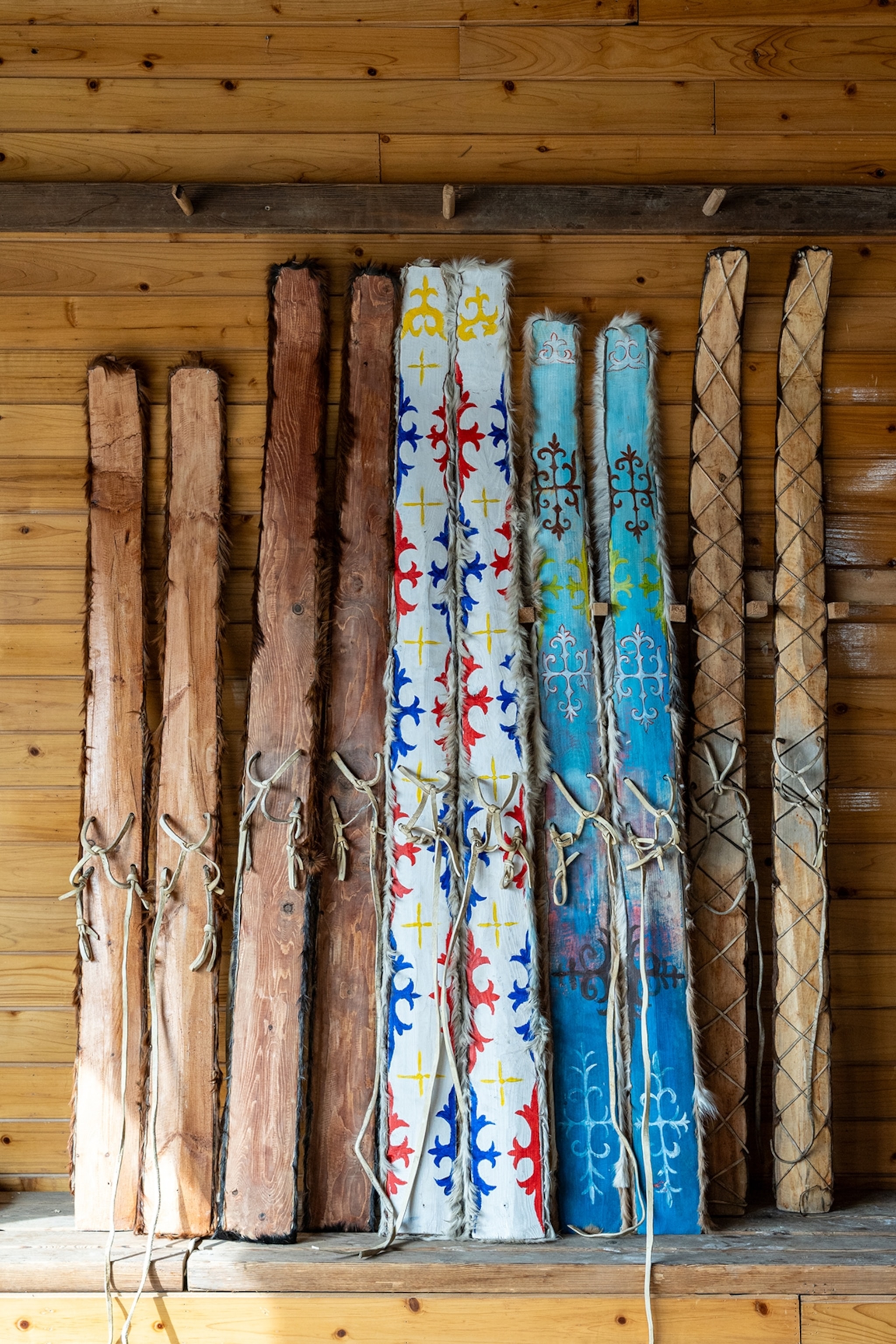 A few pairs of rustic and simple wooden skis leaning against a wooden wall.