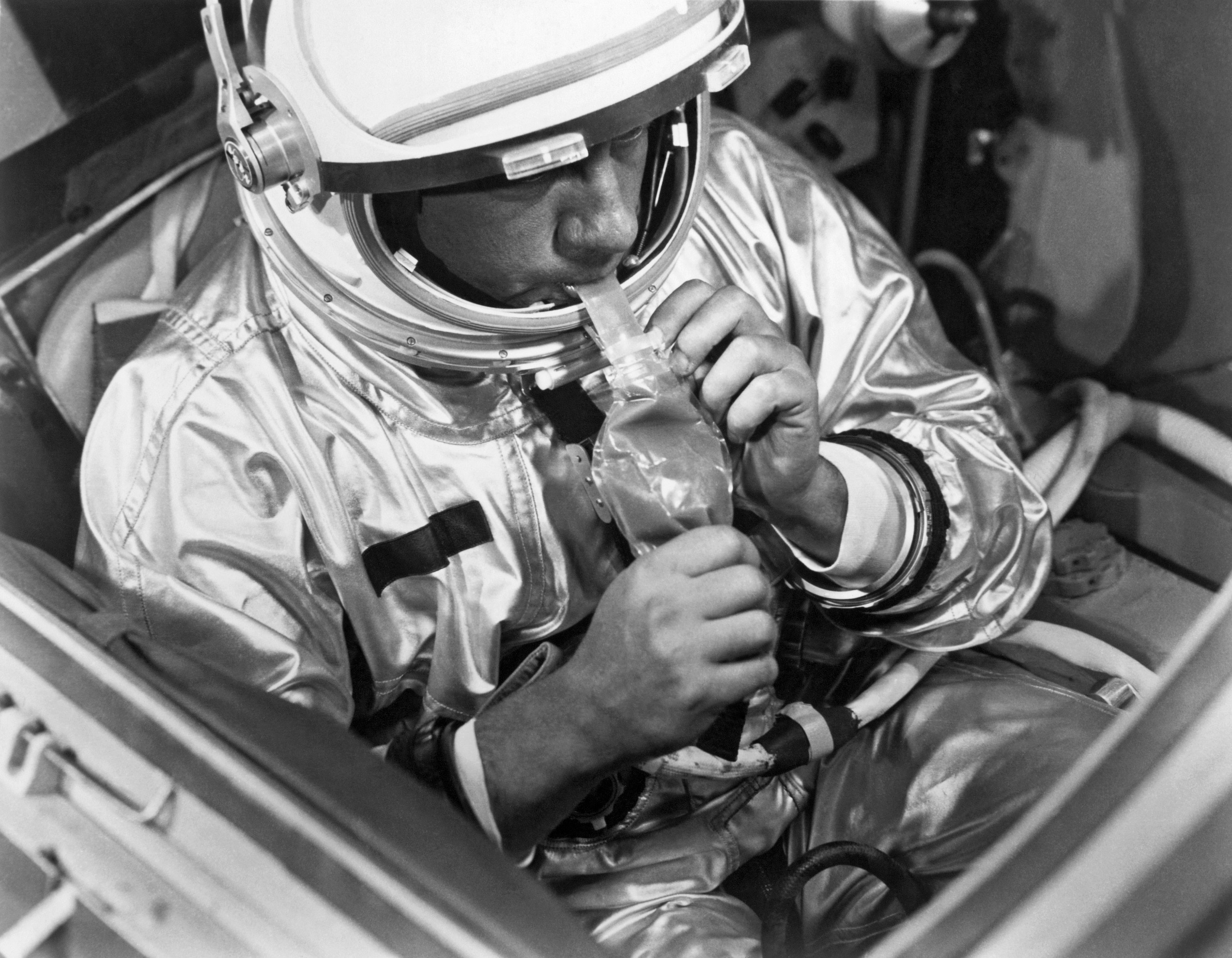 Black and white image from 1966 of test subject in Astronaut suit eating pot roast through a tube
