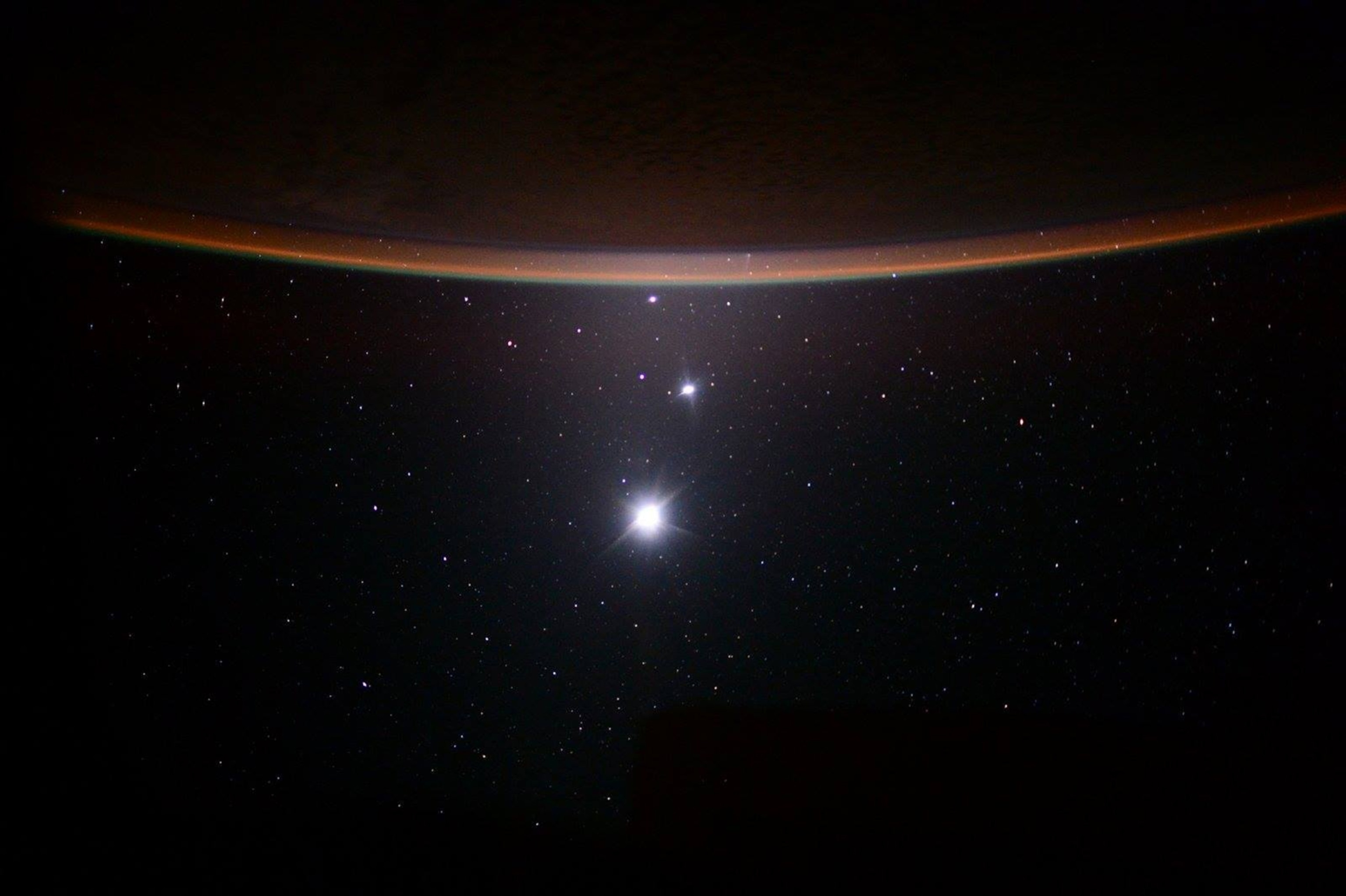 A Jupiter, Venus, and the moon aligned against a backdrop of stars and space, with Earth's glowing orange horizon arc above