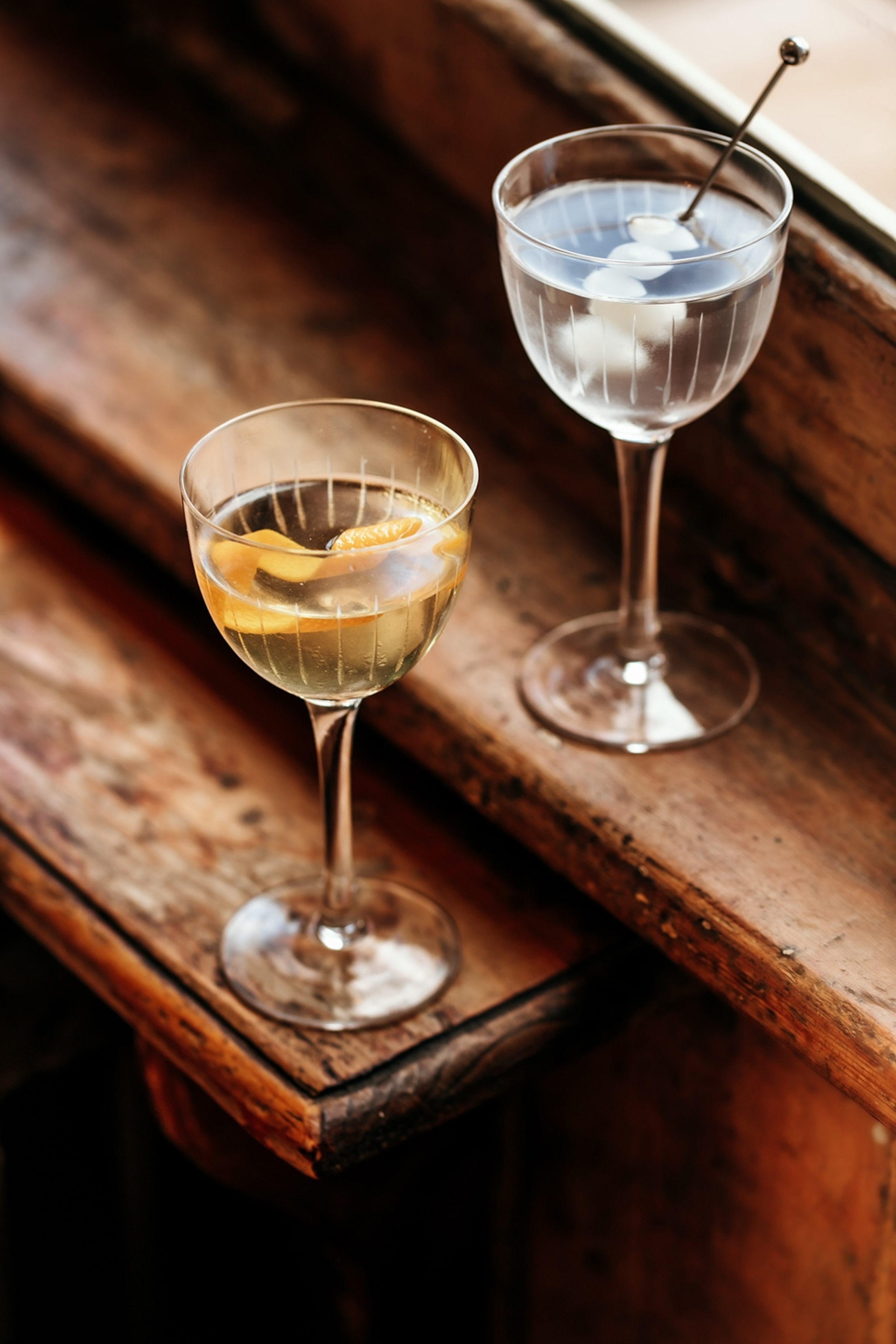 Two neat cocktails on a wooden windowsill.