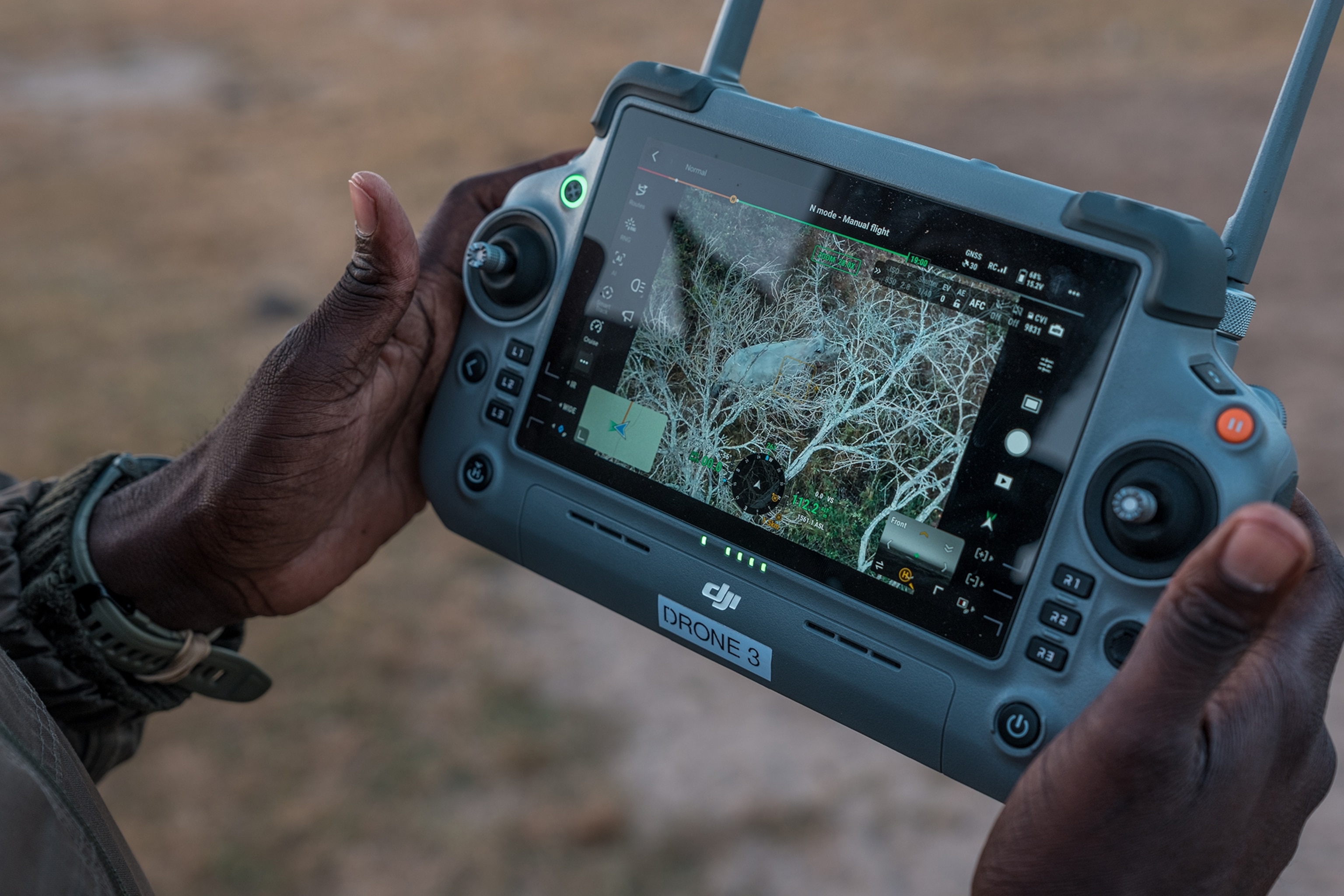 two hands holding the remote and screen for a drone. the screen shows the arial of African bush landscape with rhino