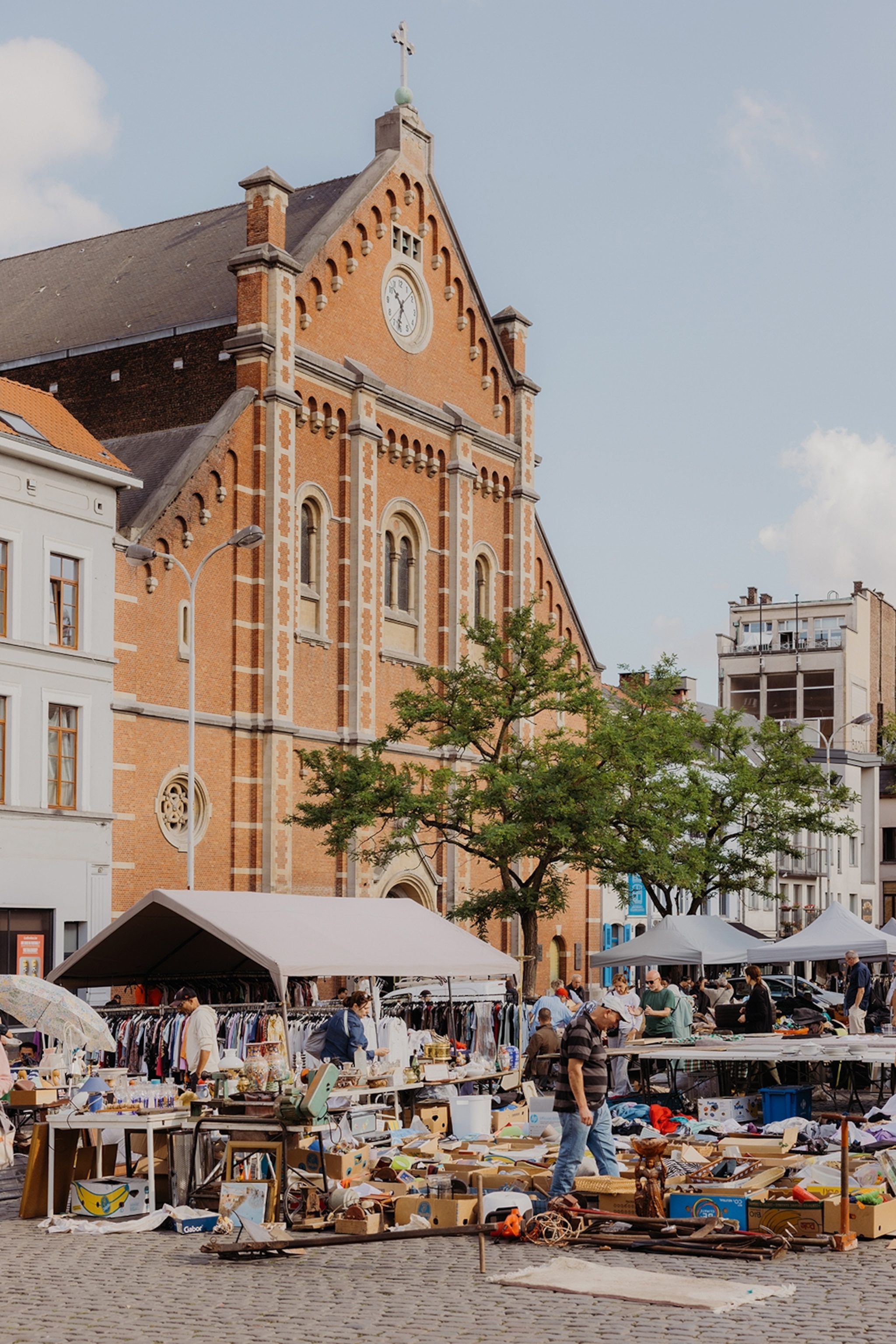 A busy, urban flea market on a cobble-stoned plaza in front of a simple brick building.