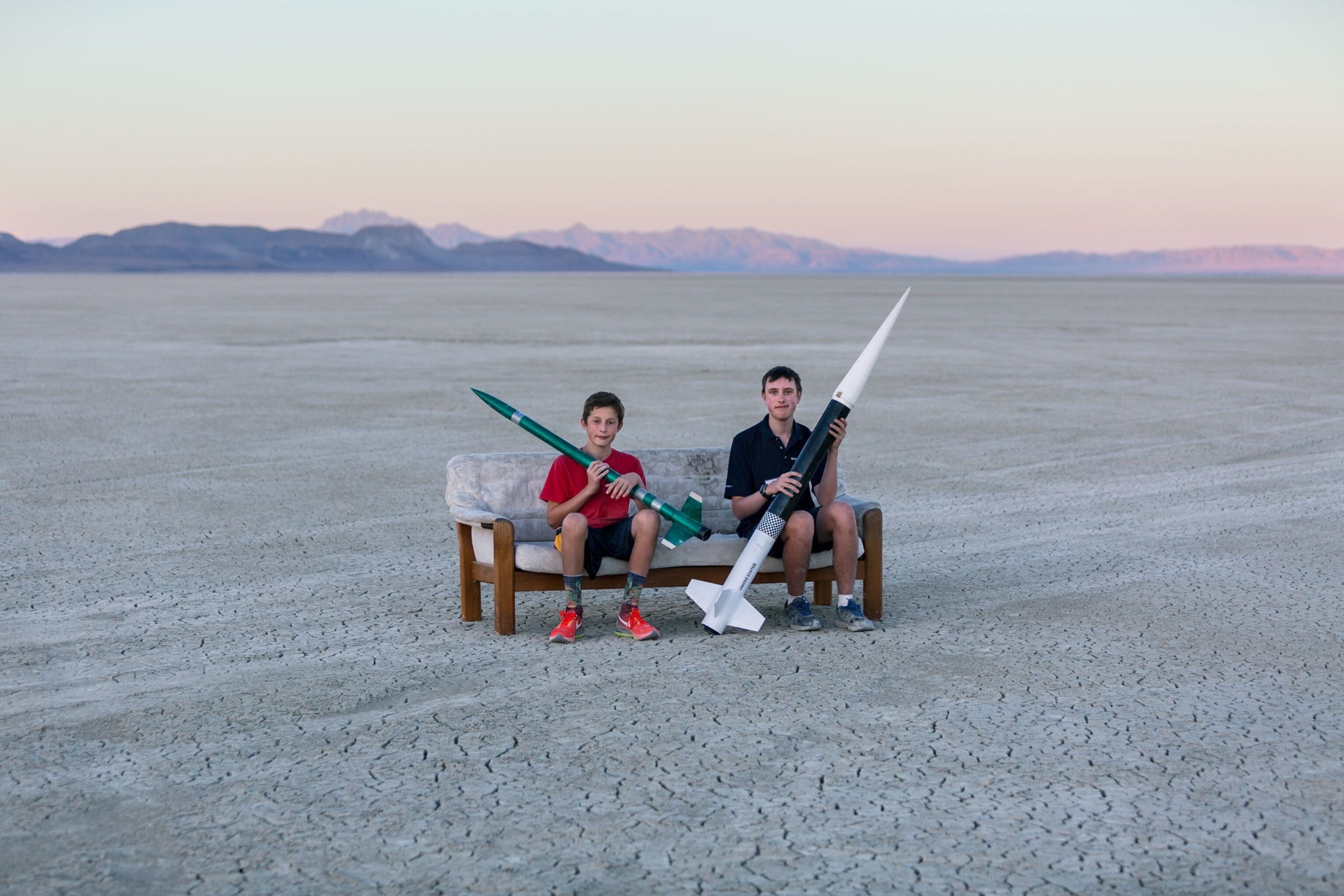two young boys sitting on a couch in the desert each holding a rocket during sunset
