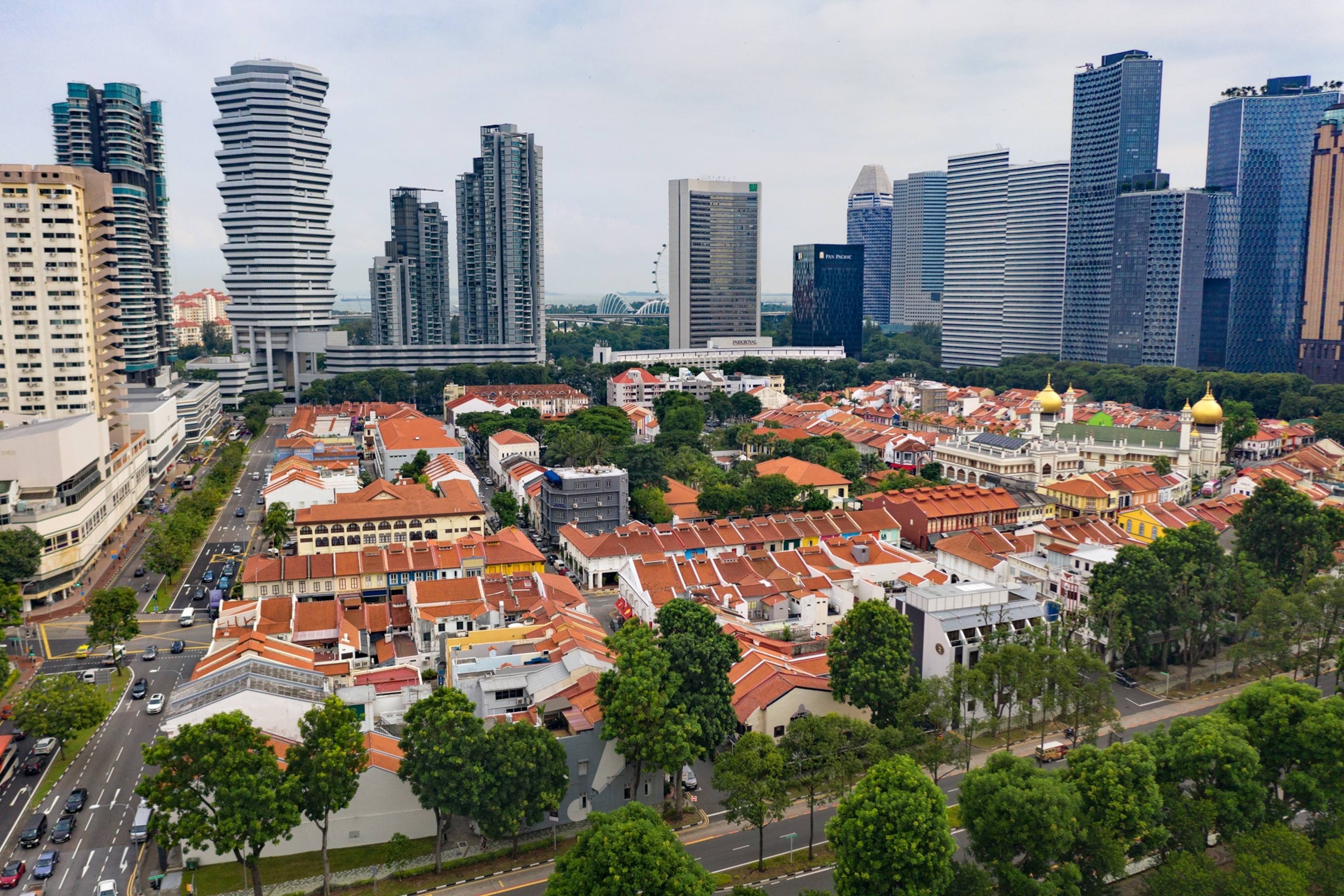 an aerial view of white buildings with red roofs surrounded by trees and hi-rises