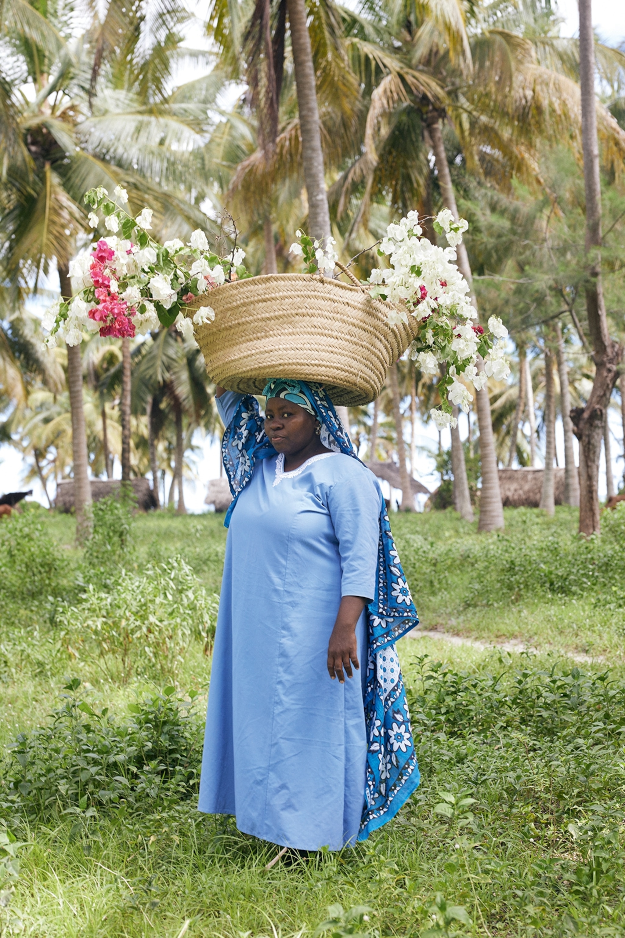 A local woman posing for a portrait in a tropical garden, balancing a woven basket on her head.