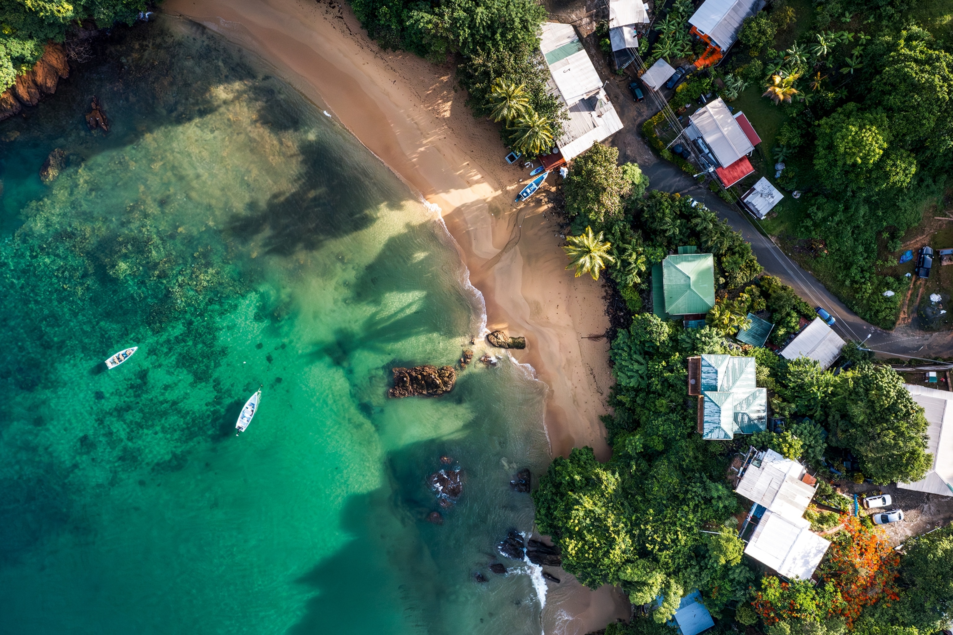 A crystal-clear bay with small fishing boats and houses bordering the sand beach.