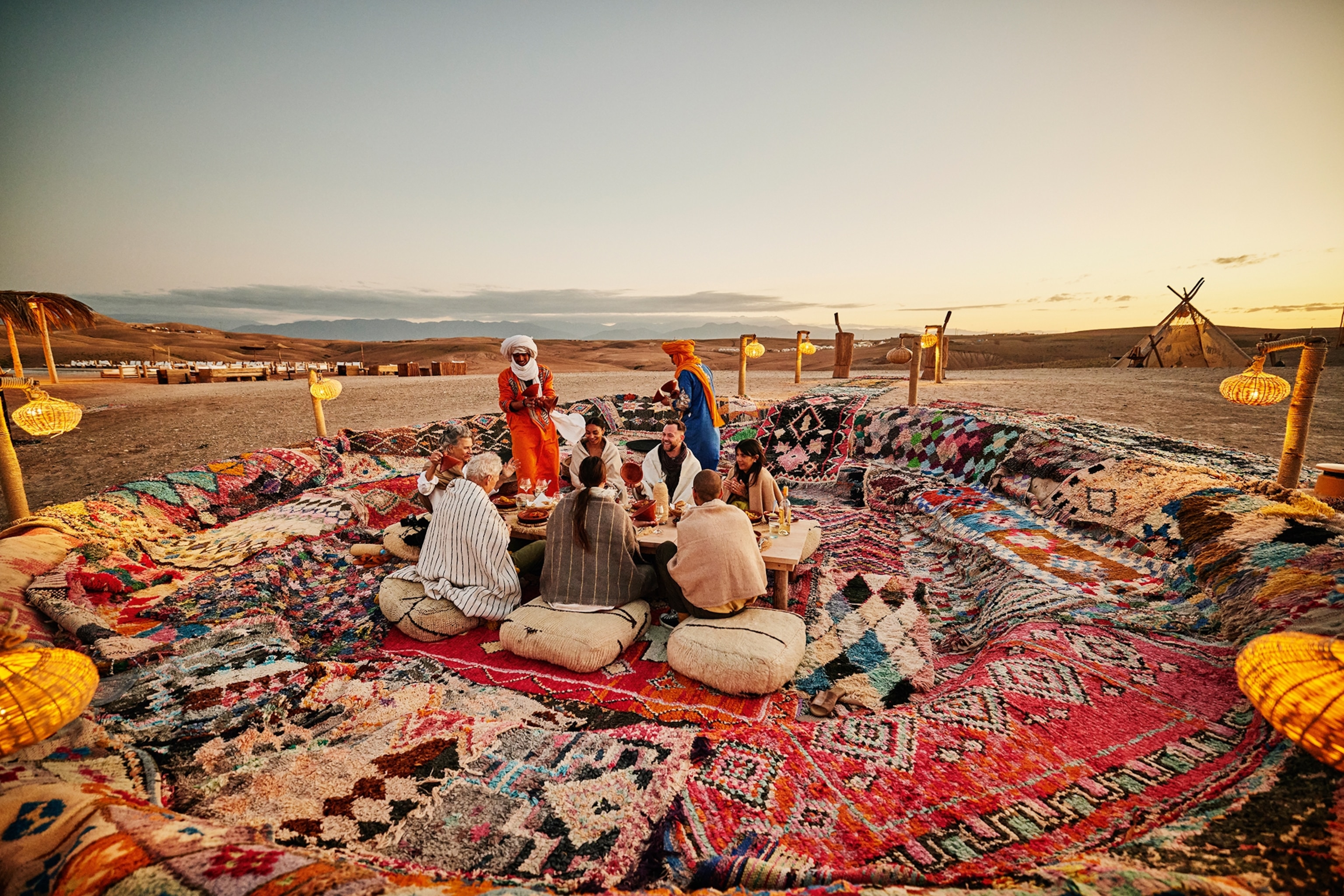 A group of tourists sitting on rugs in a pit in the desert as local guides play music.