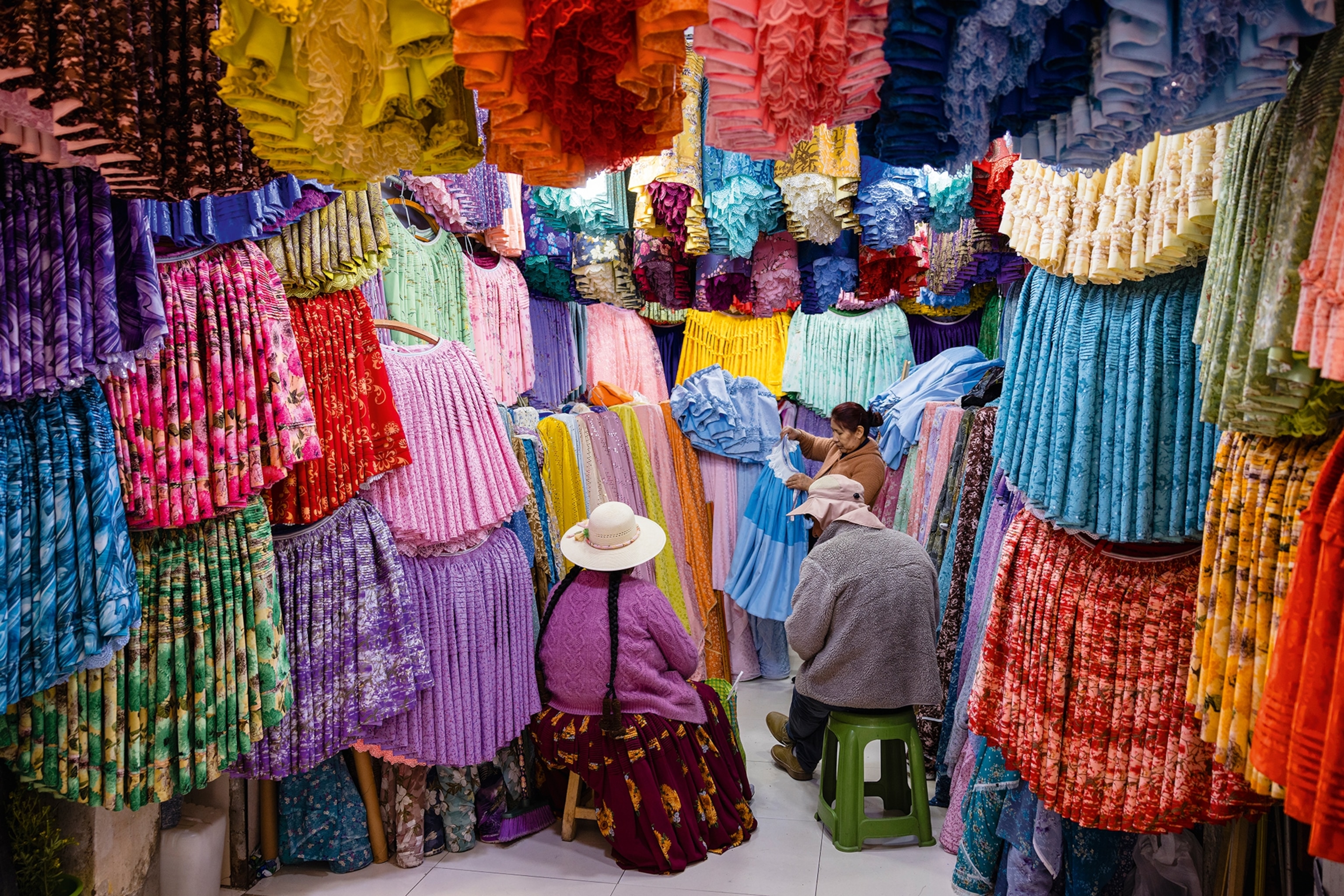 The interior of a market shop with puffy skirts hung on the walls, while a woman sits in the centre.