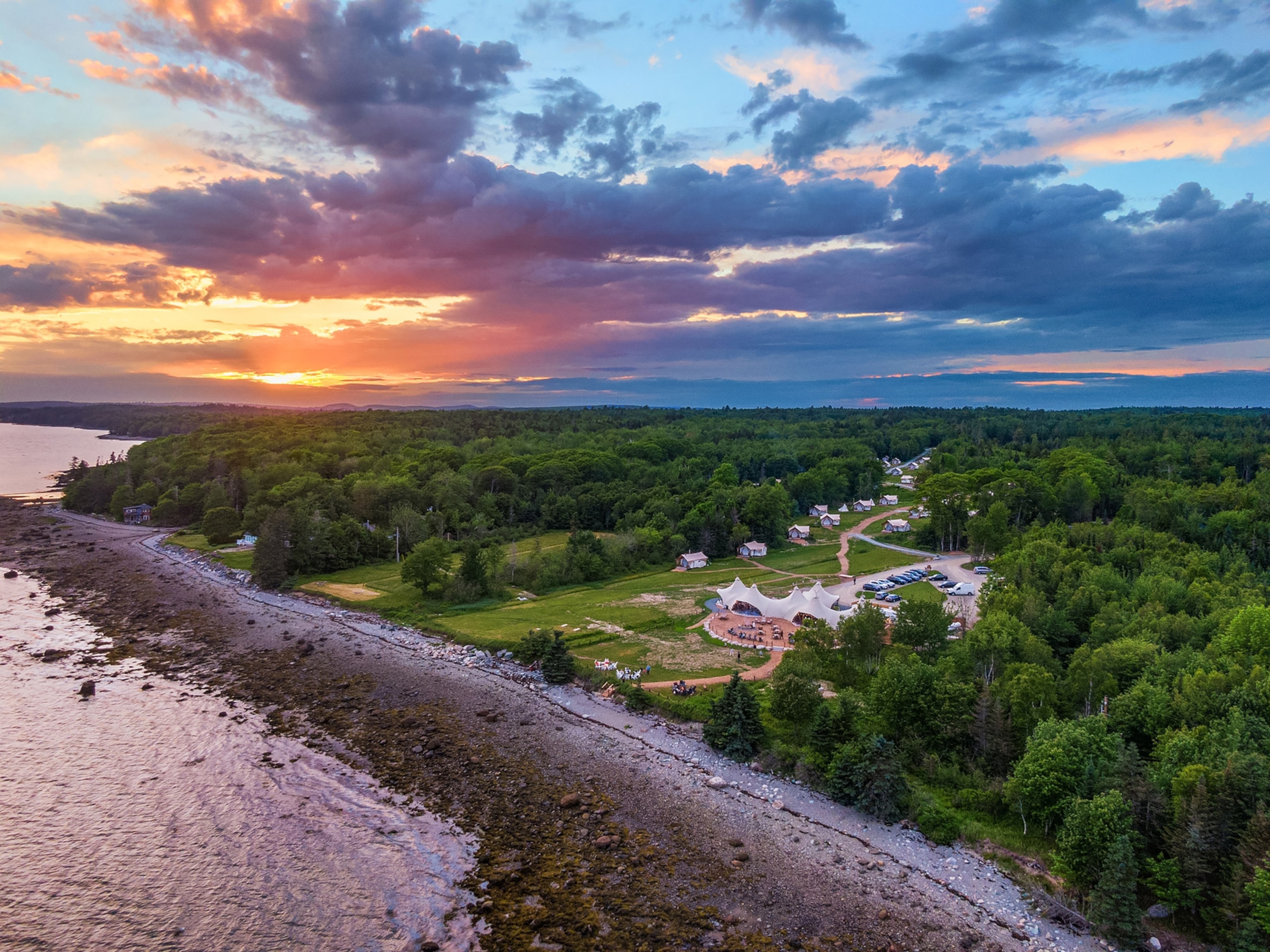 An aerial view of a luxury campsite next to a beach, surrounded by dense trees