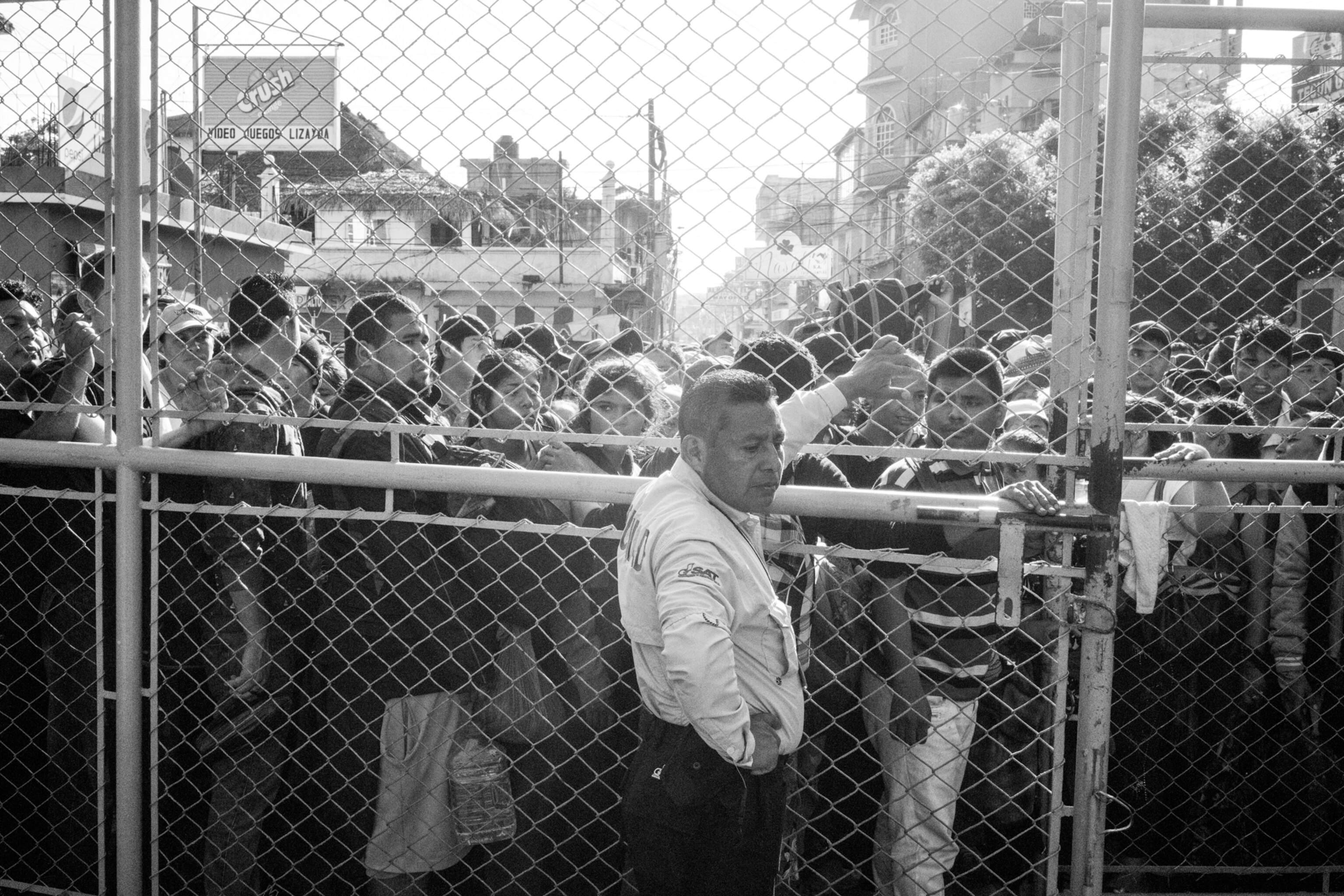a police officer leaning against a fence with men waiting behind the fence