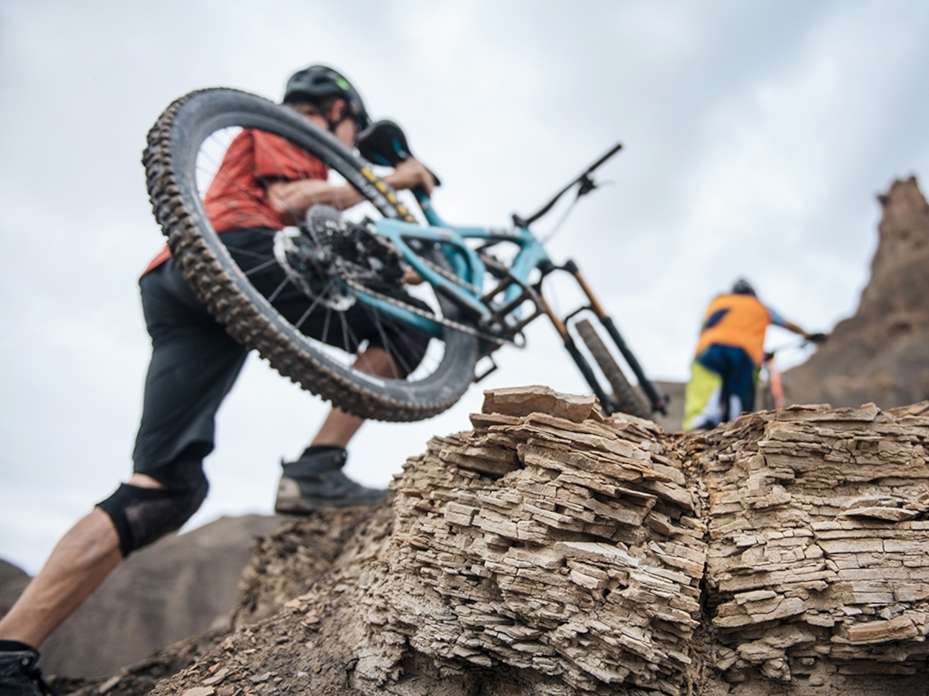 two mountain bikers hiking with their bikes on their shoulders up a steep embankment.