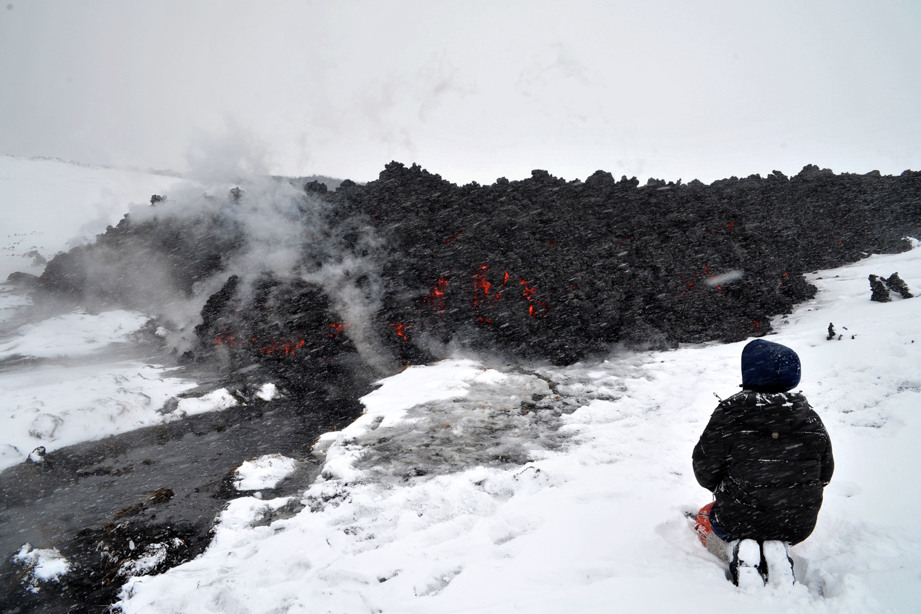 someone watching steaming meltwater emerge from underneath a lava flow