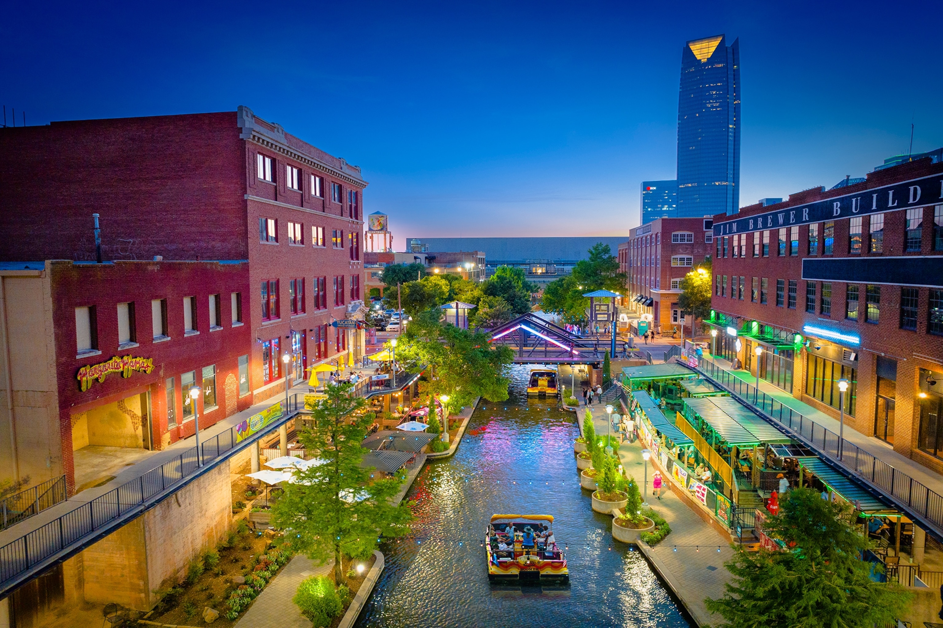 A boat travels down a canal surrounded by large, red-bricked buildings in Oklahoma City's Bricktown district.