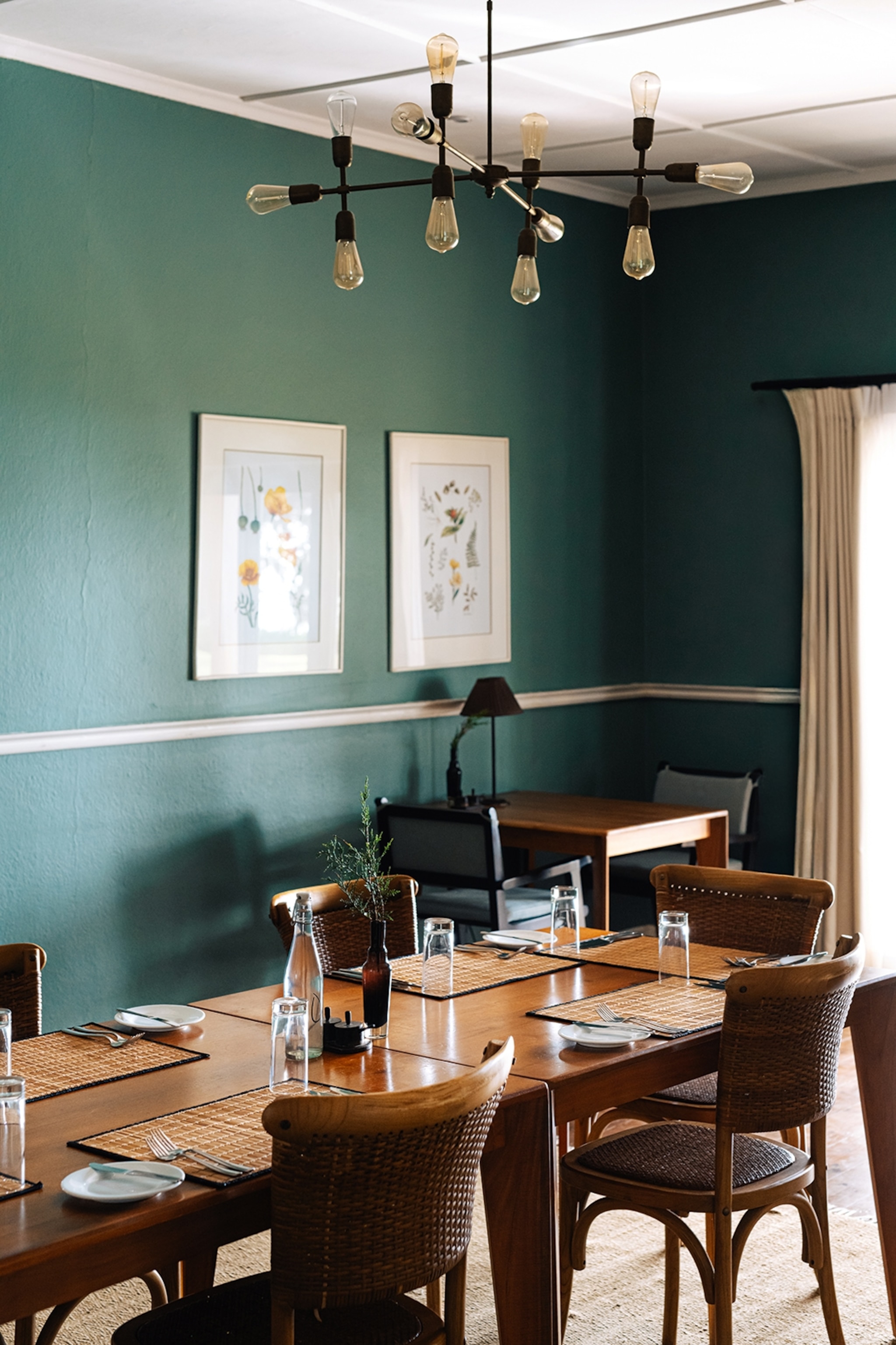 The interiors of a sleek dining room in a hotel, decorated in the mid-century style with curved teakwood furniture and muted colours.