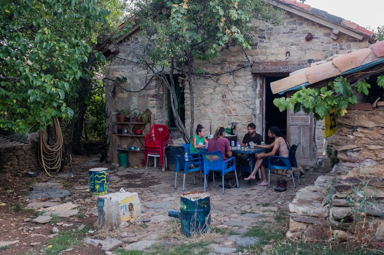A group of people sit in front of a community house and kitchen.