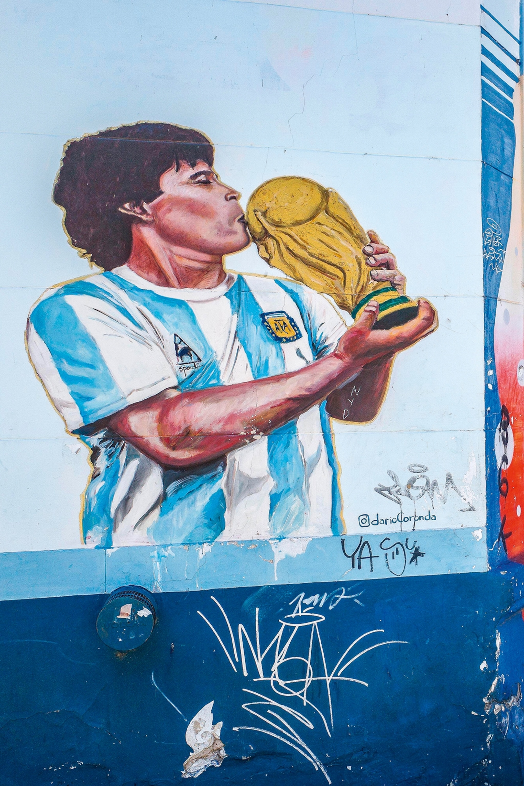 A mural with a male football player kissing a Fifa cup trophy on the side of a street wall.