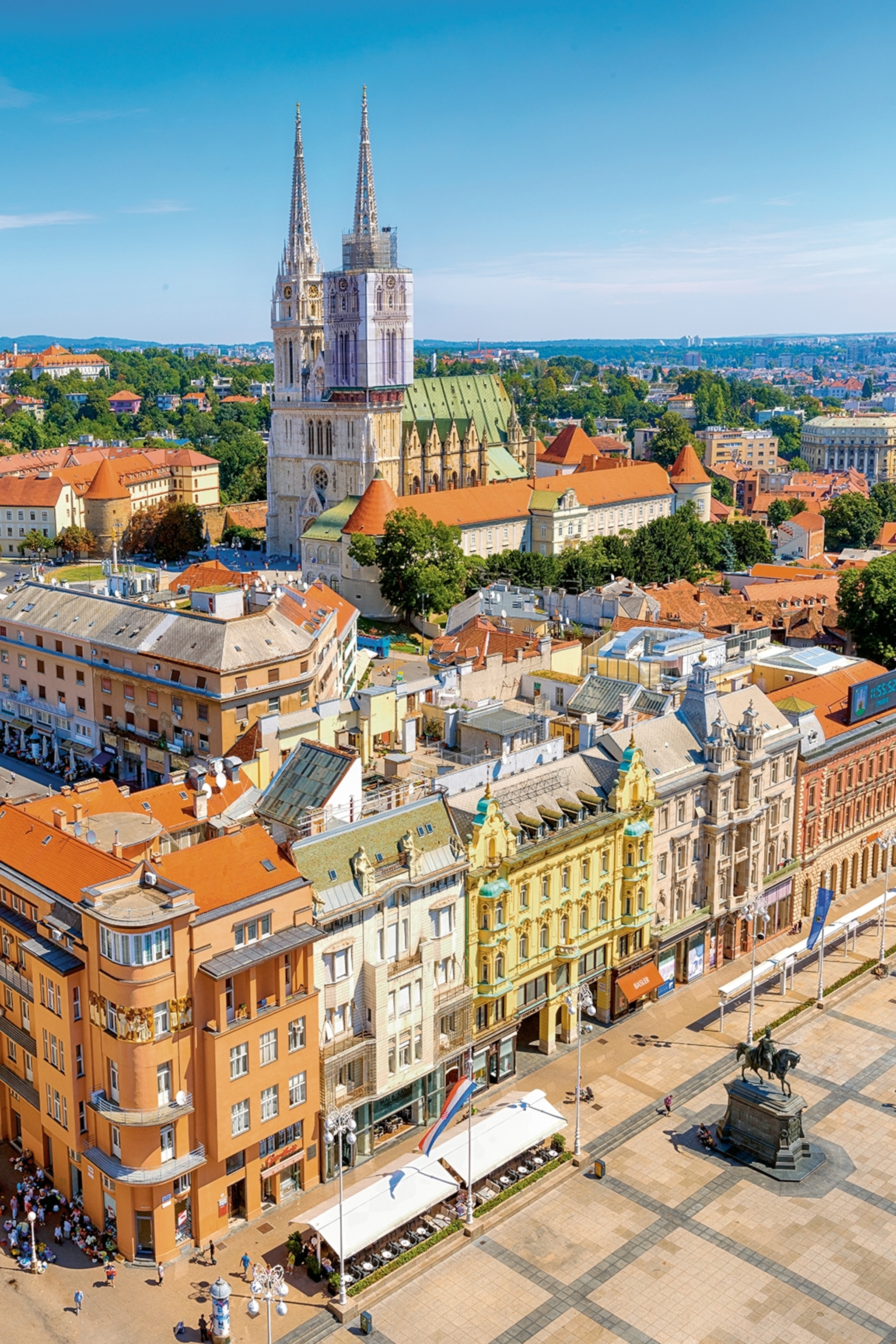 A vibrant city square photographed from the air with a cathedral in the distance.