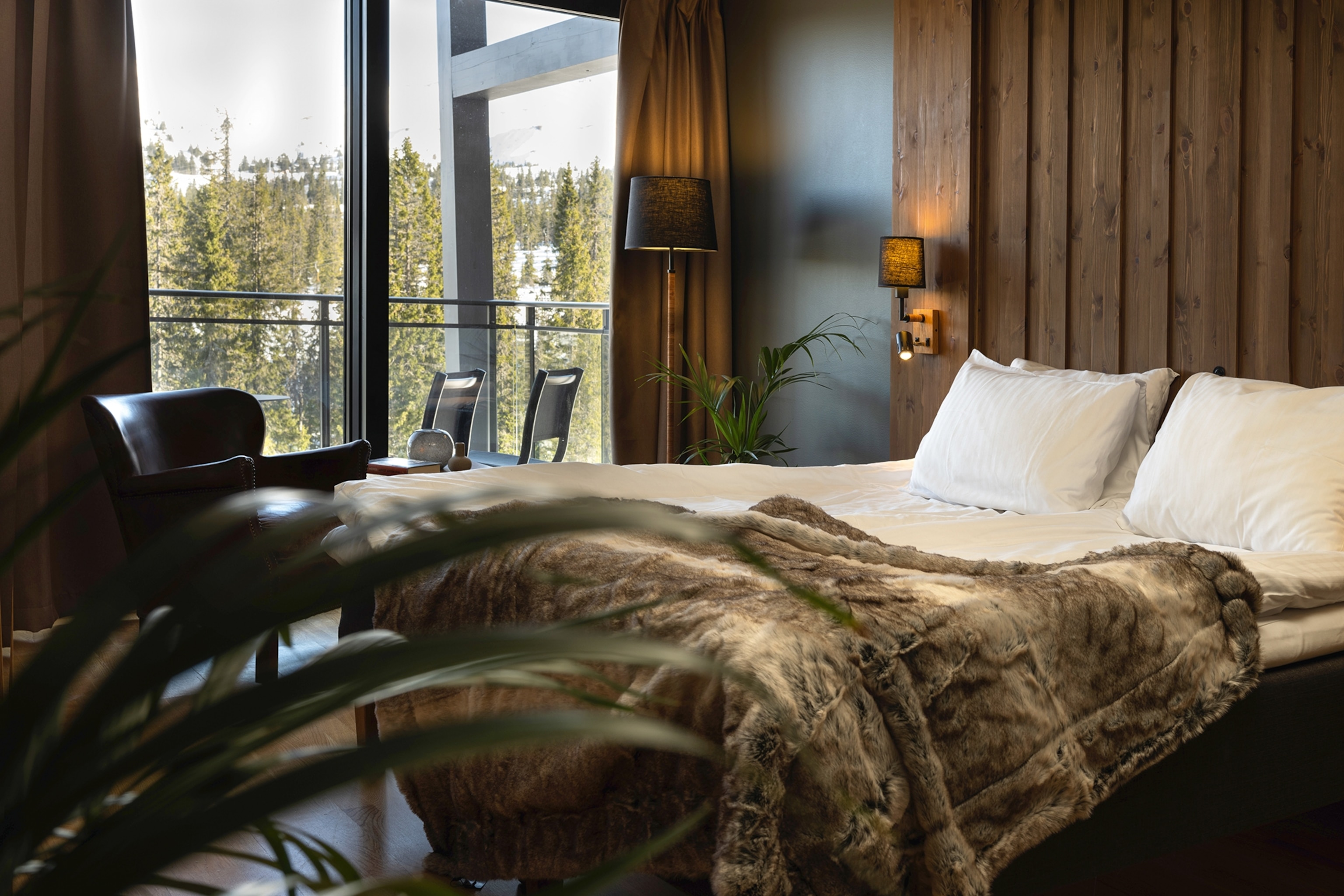 The interiors of a skiing lodge with wooden panels and a double bed with a fur blanket draped across.