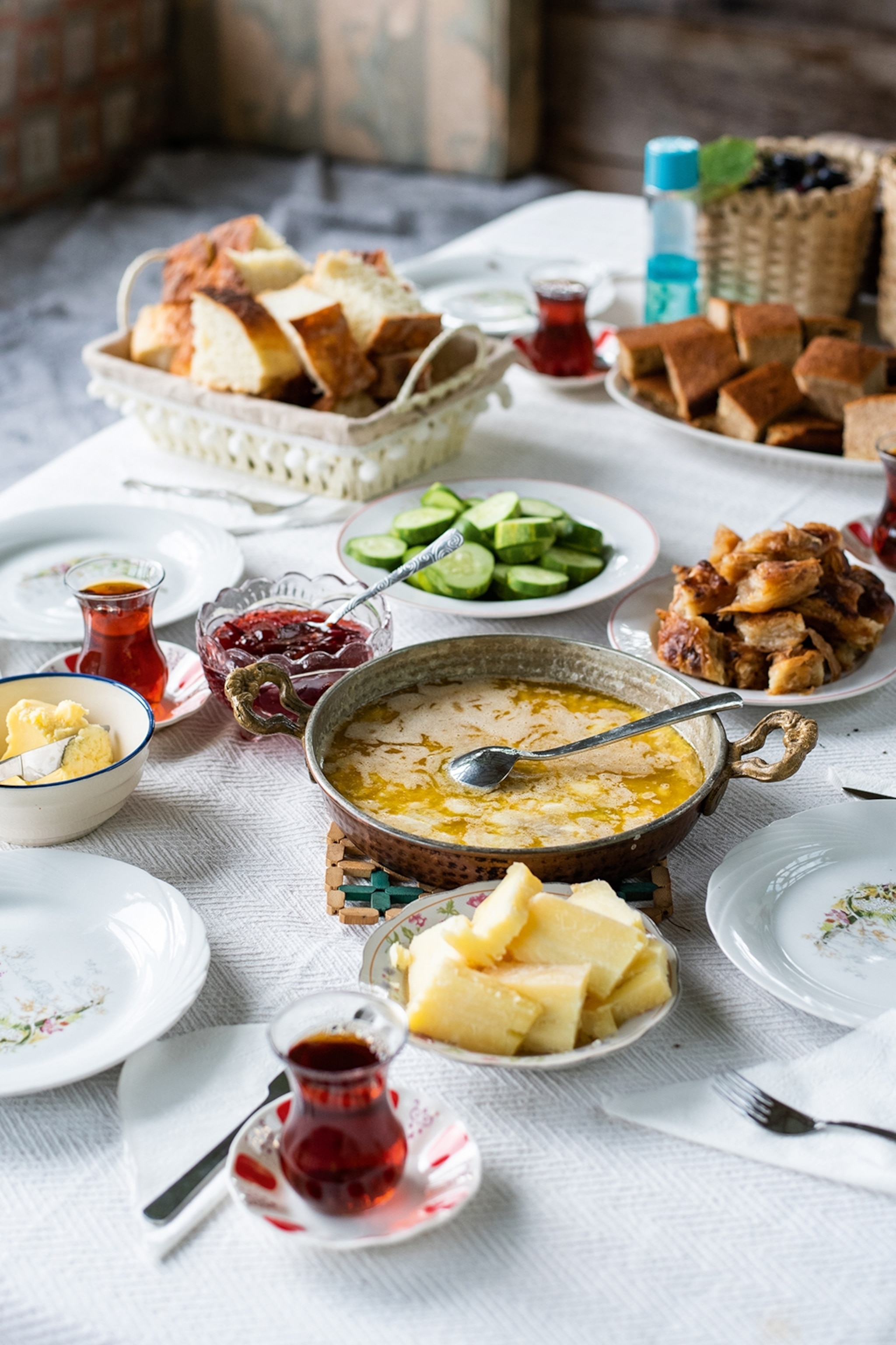 A spread of dishes and tea on a white-clothed table, including cut cucumber, bread and a cheesy dip.