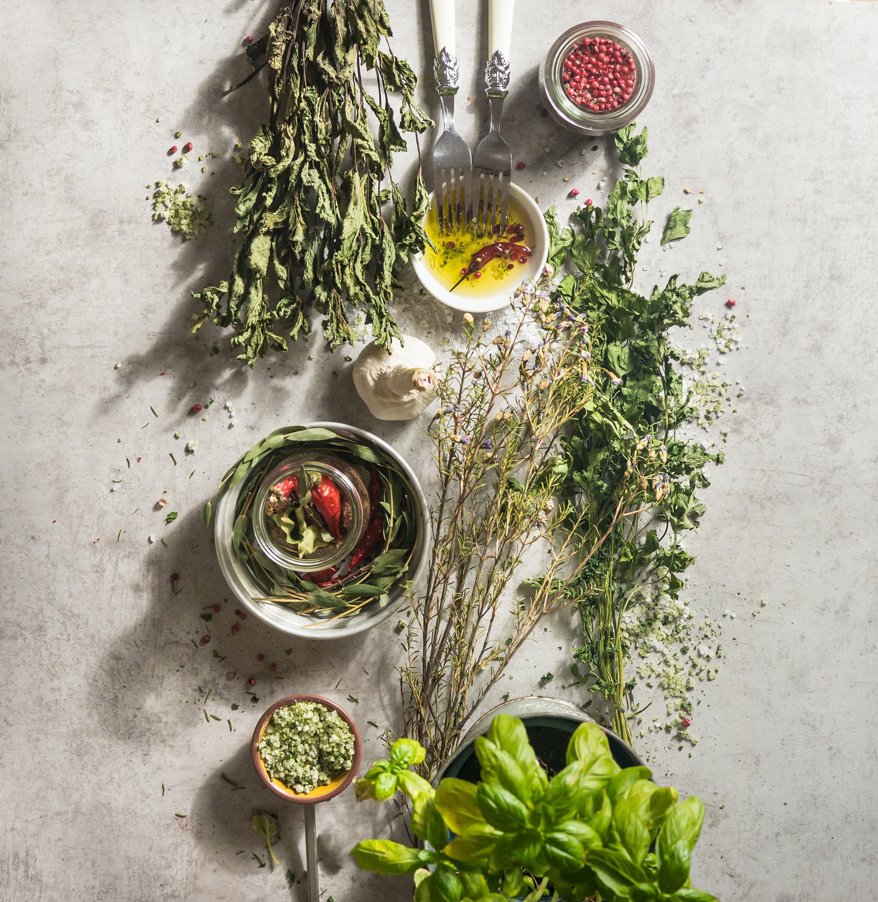 Various kitchen flavor herbs on pale concrete kitchen table with bowls, forks, and spices