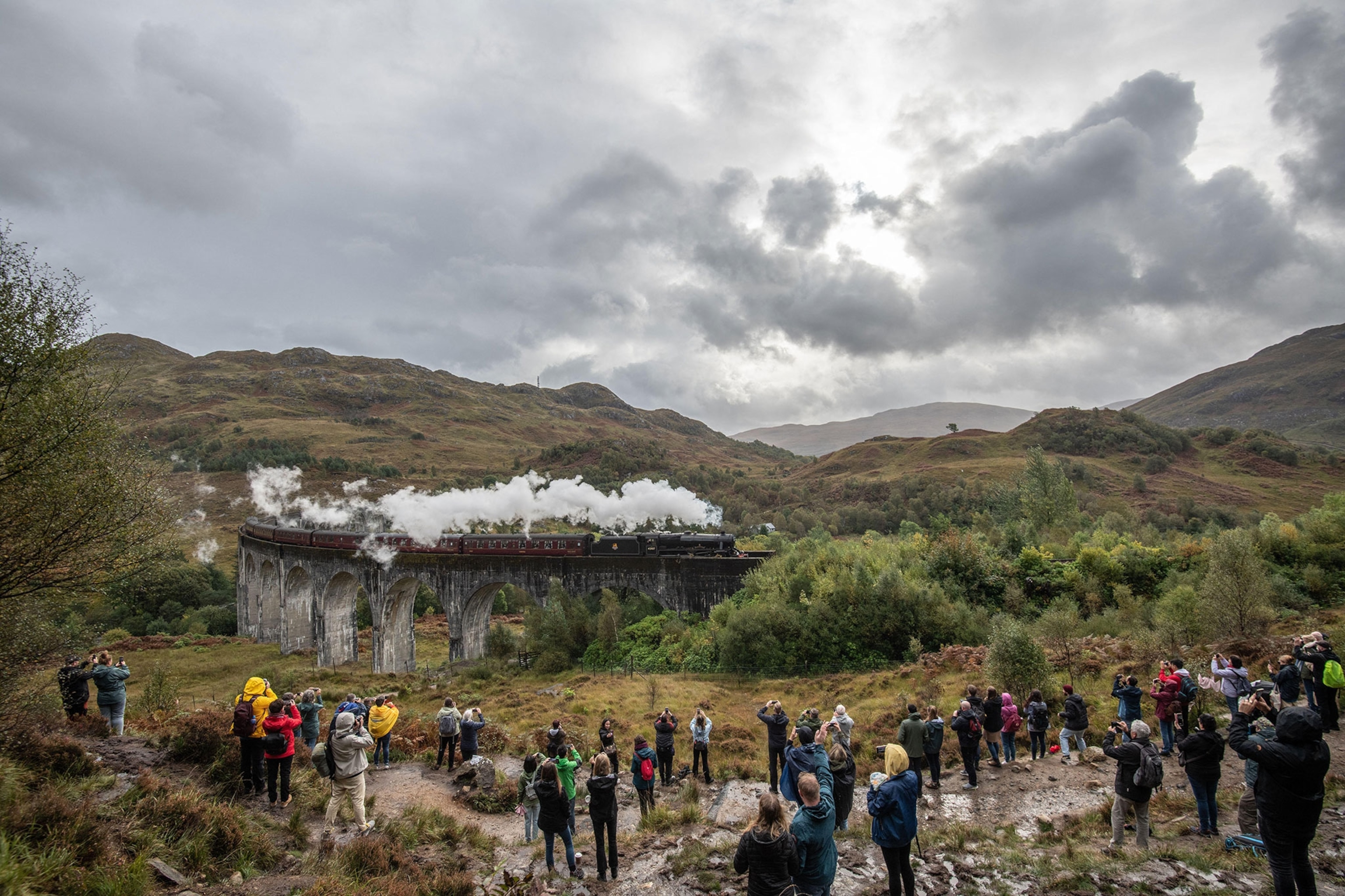 The Jacobite Steam Train, also known as the Hogwarts Express, featured in the Harry Potter Films, goes over the Glenfinnan Viaduct on the west Highland Line, as crowds of onlookers watch.
