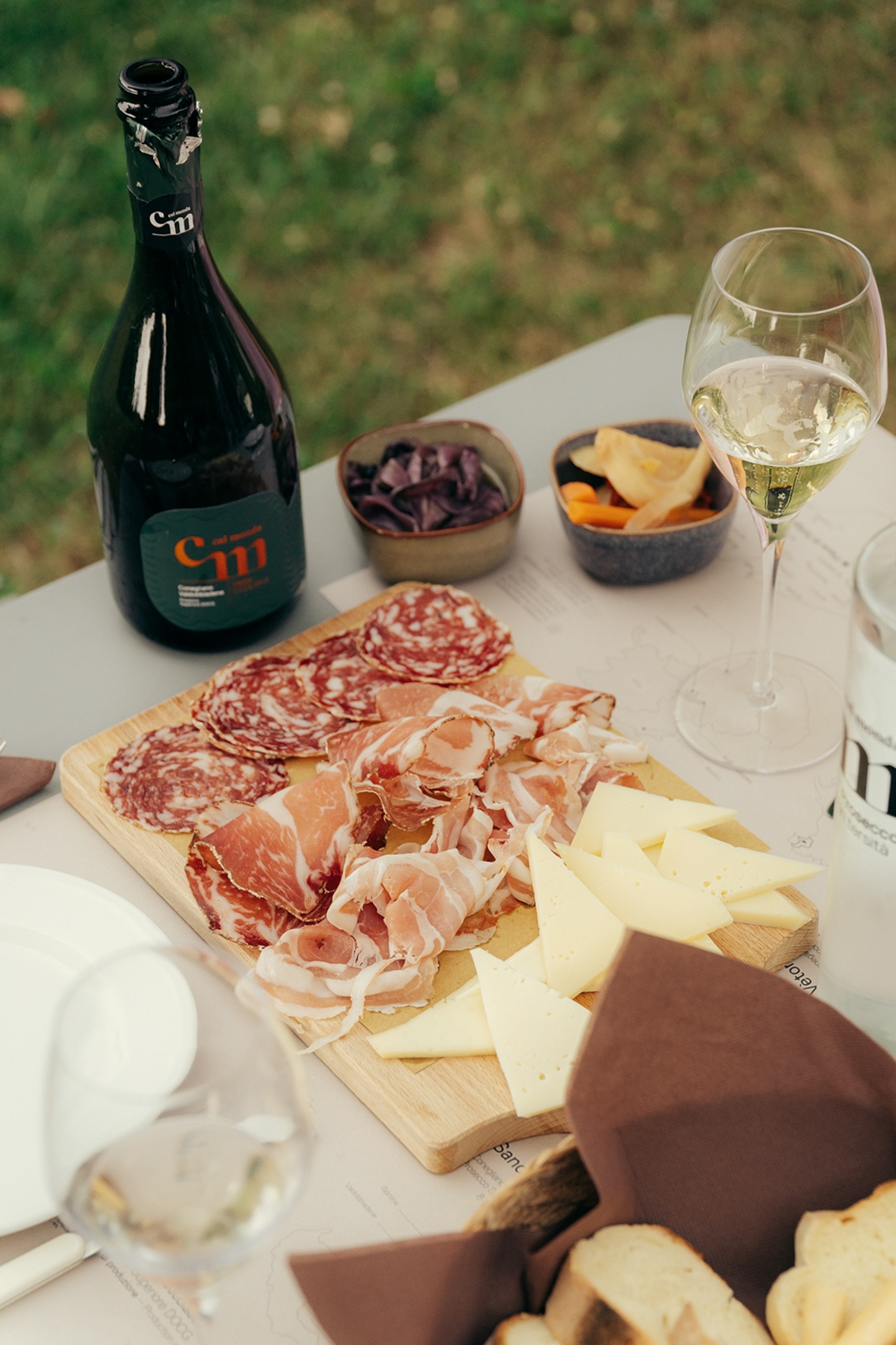 An outdoor table set with a charcuterie board featuring cheeses and cured meats alongside a bottle of Prosecco.