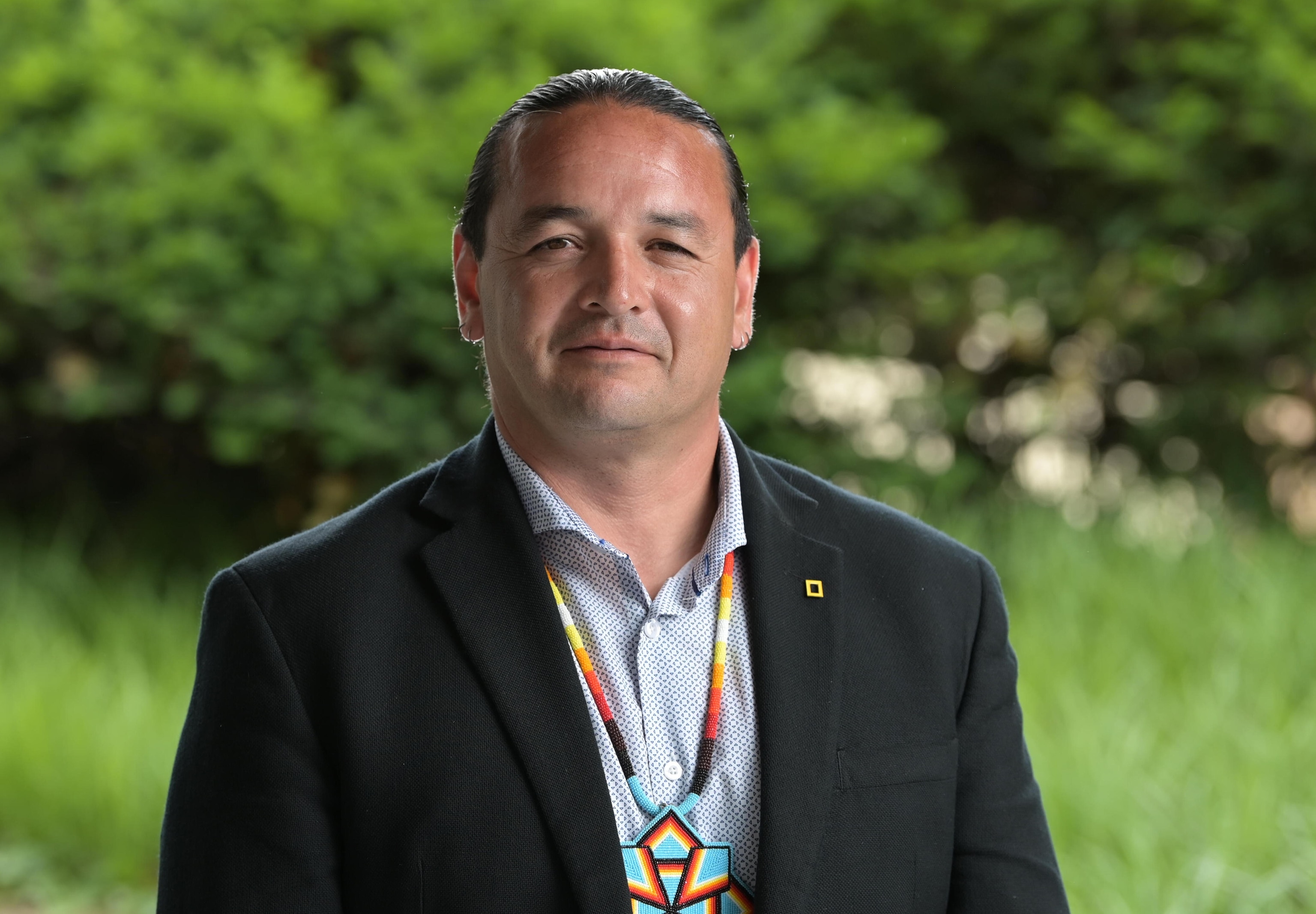 Indigenous ecologist and National Geographic Explorer Jason Baldes in front of green foliage.