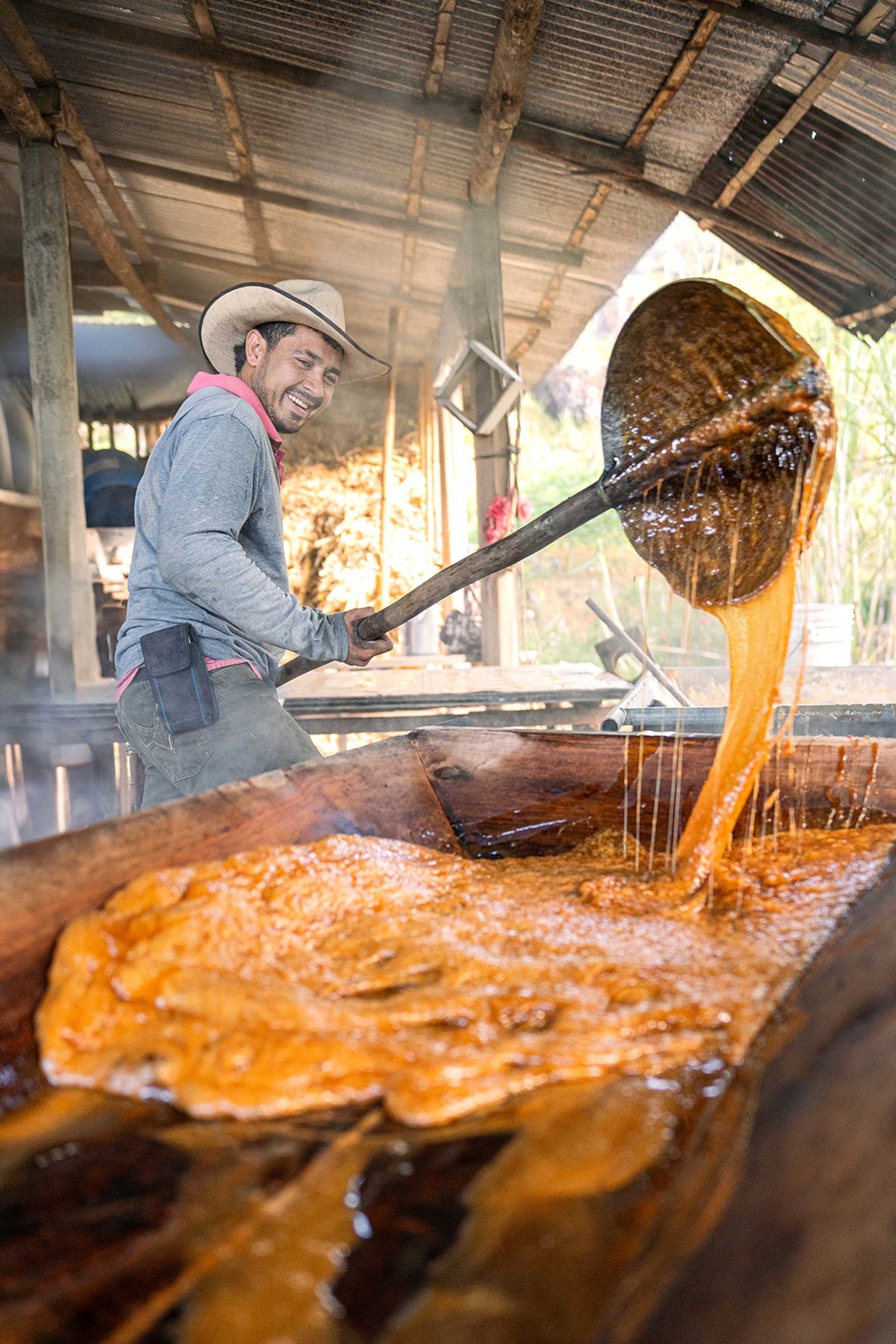 A middle-aged man mixing hot sugar-cane caramel and holding up a big spoon with the mass dripping off.