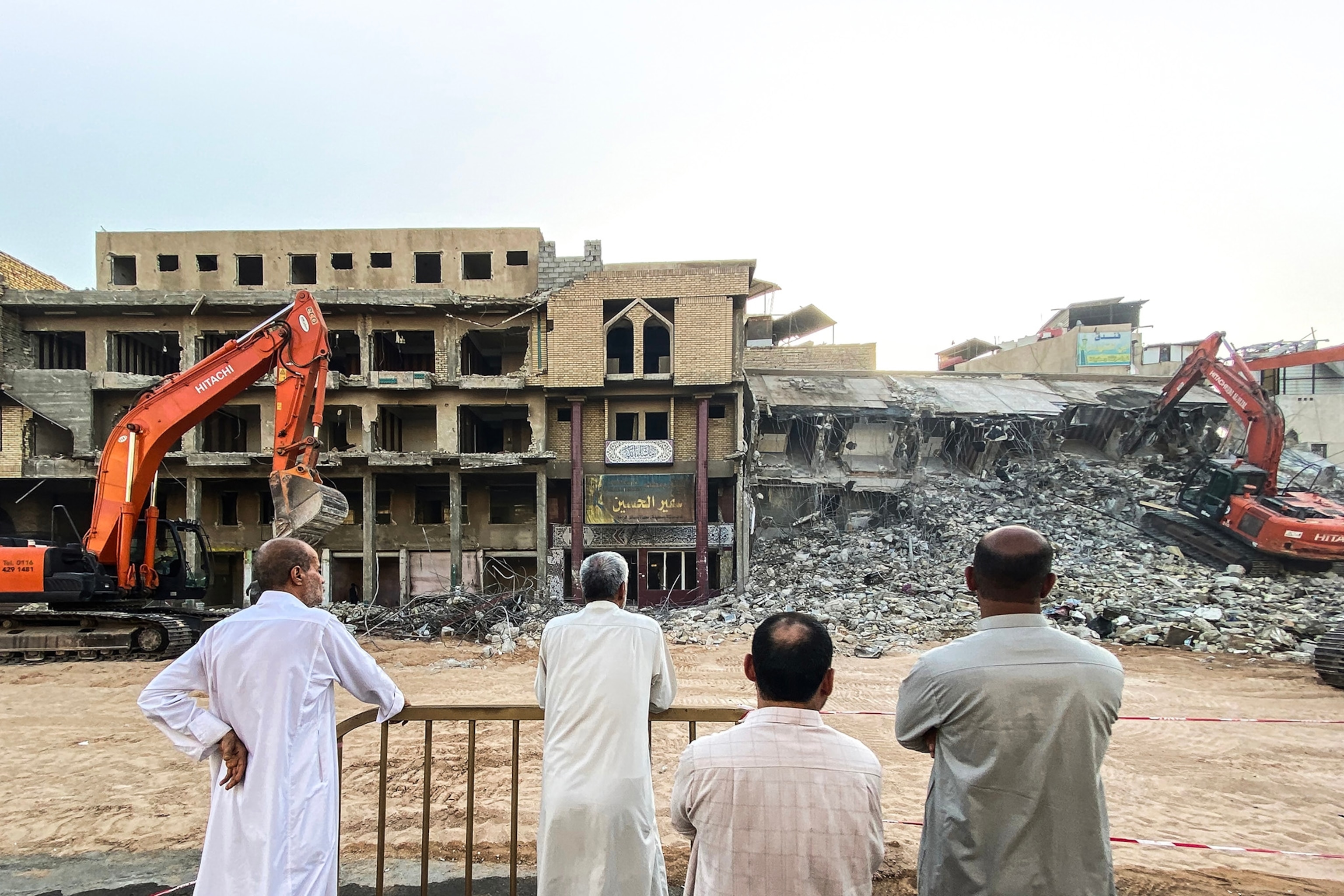 Four men stand watching buildings being torn down