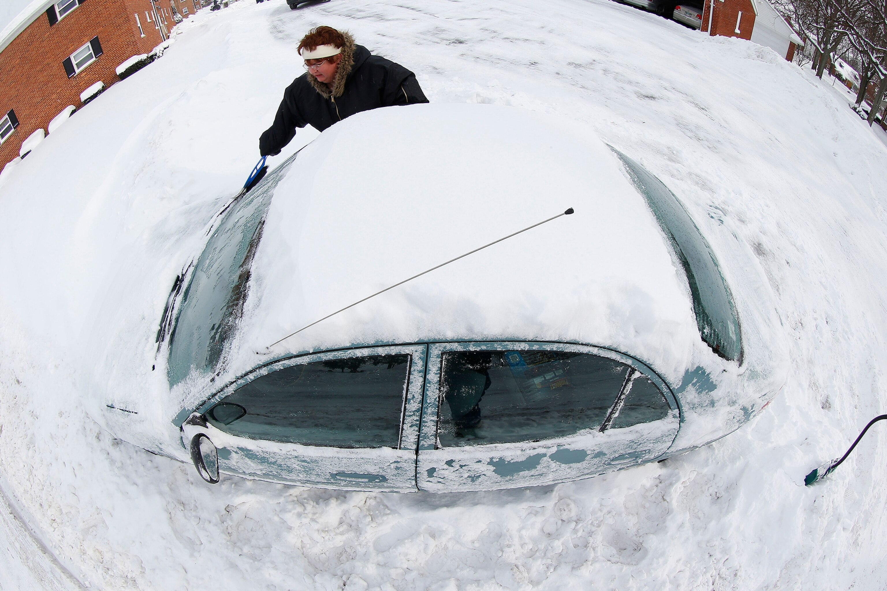 a woman digging out her car from a mountain of snow.
