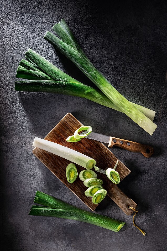 Whole and cut leeks on a wooden serving board.