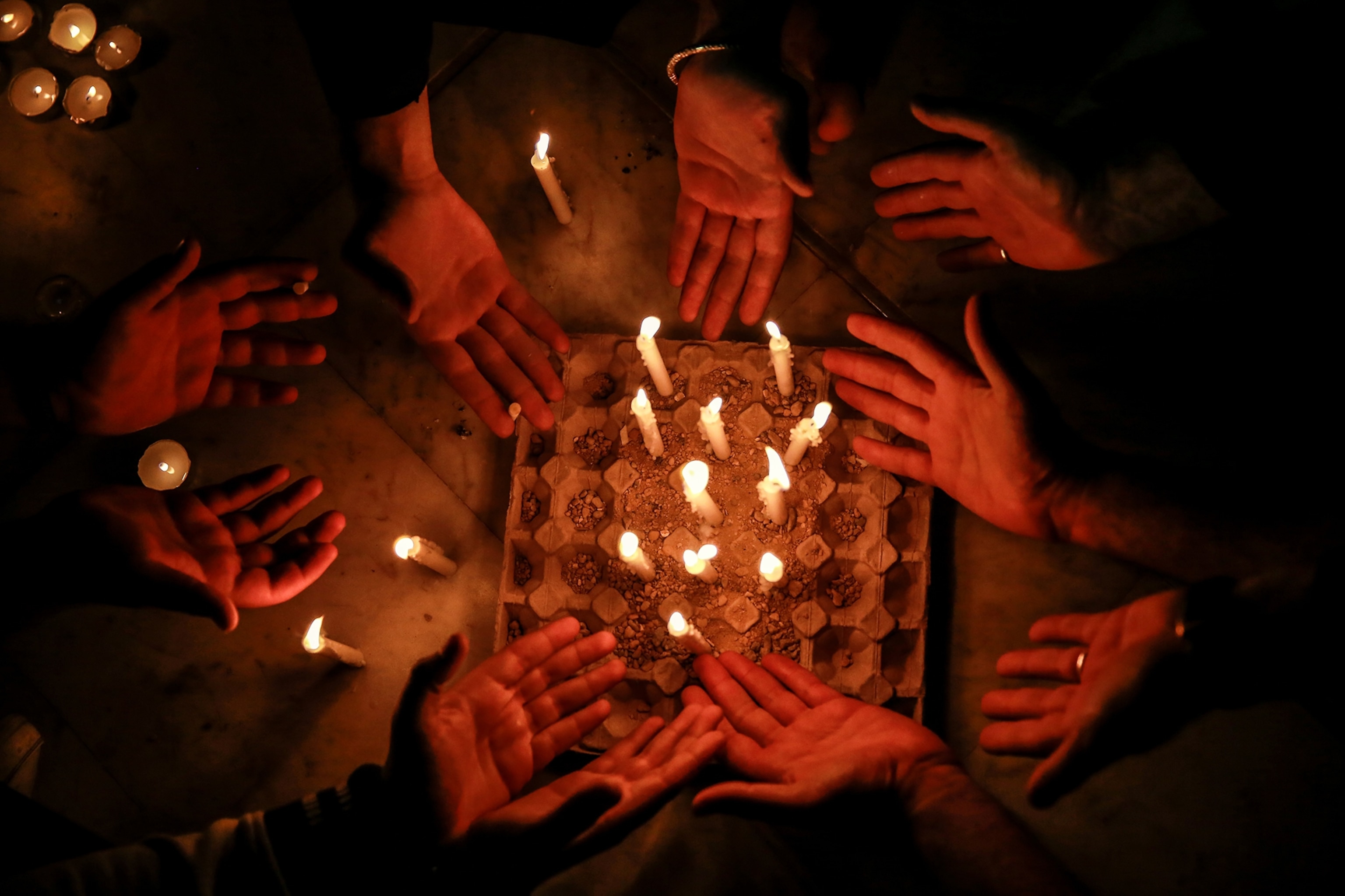 A circle of hands reach towards candles